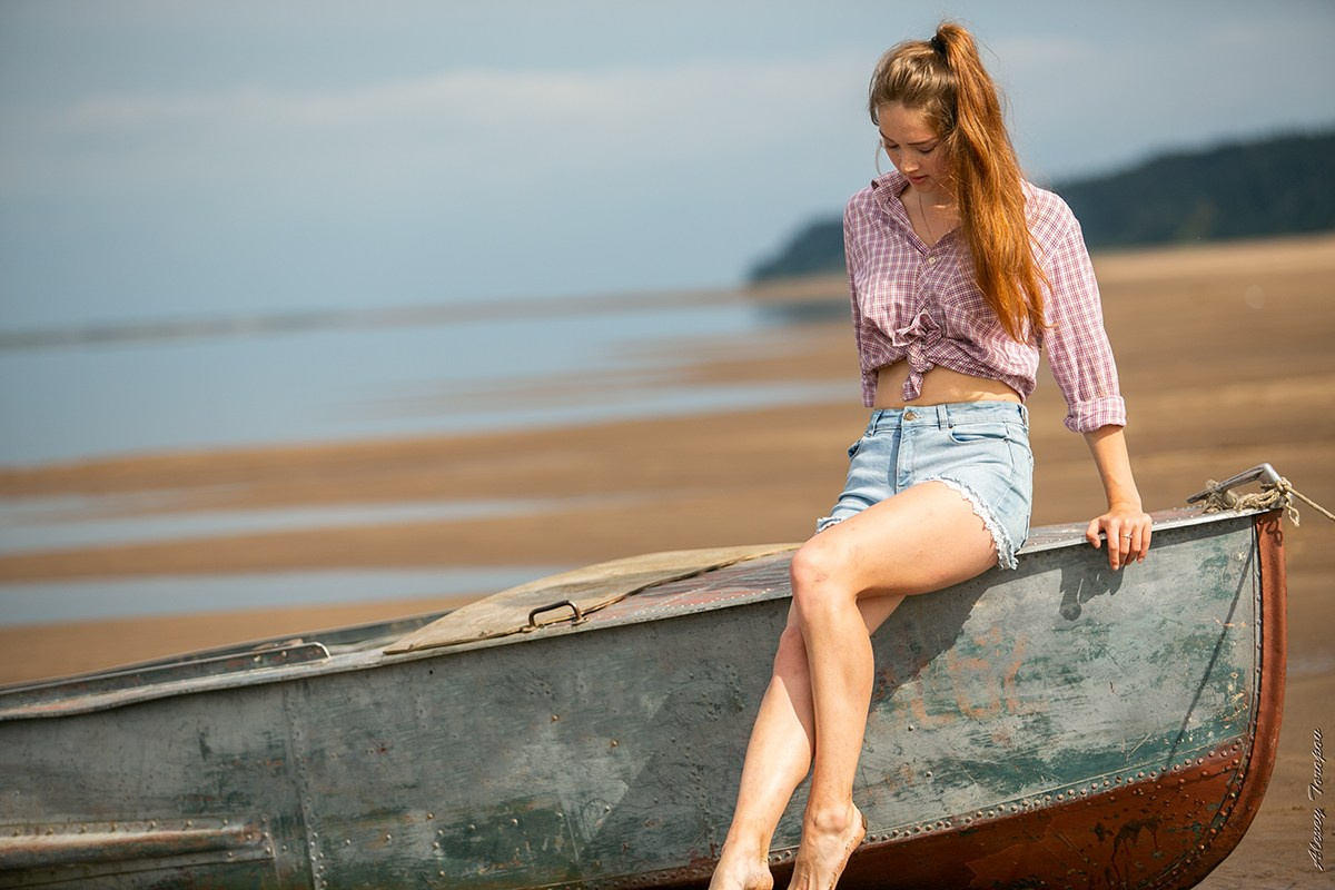 Девушка в шортах позирует на старой лодке на берегу реки