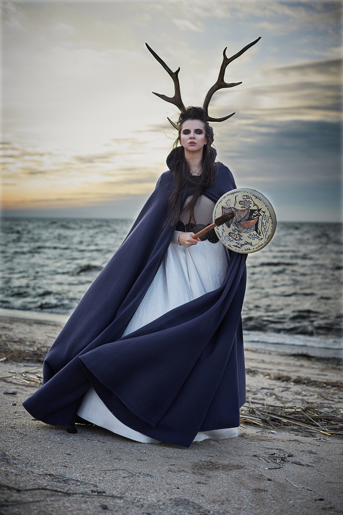 Художественная съемка на берегу моря. Девушка в образе шамана с оленьими рогами, накидка развевается на ветру, в руках бубен. Фотограф. Тимашевск. Кубань. Краснодарский край.