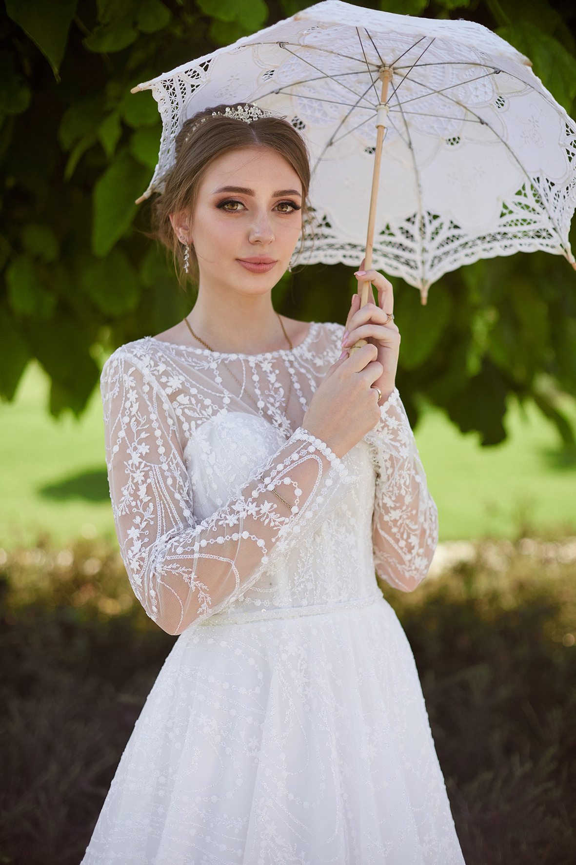 Невеста с белым зонтиком от солнца стоит под деревом в зеленом парке. Фотограф. Кубань. Краснодарский край. Тимашевск.