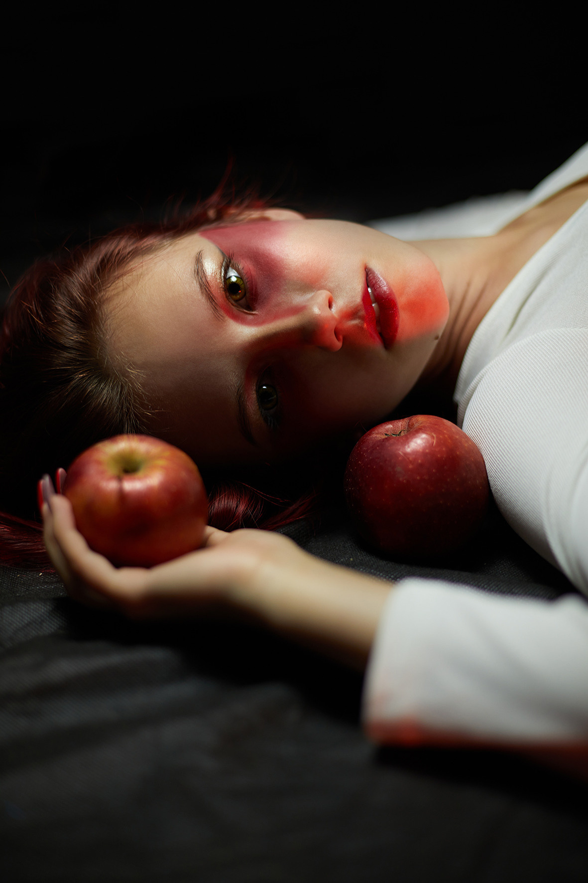 Девушка с красными волосами в белом боди лежит на черном фоне с красными яблоками. Красный макияж. Фотограф. Краснодарский край. Тимашевск. Кубань.