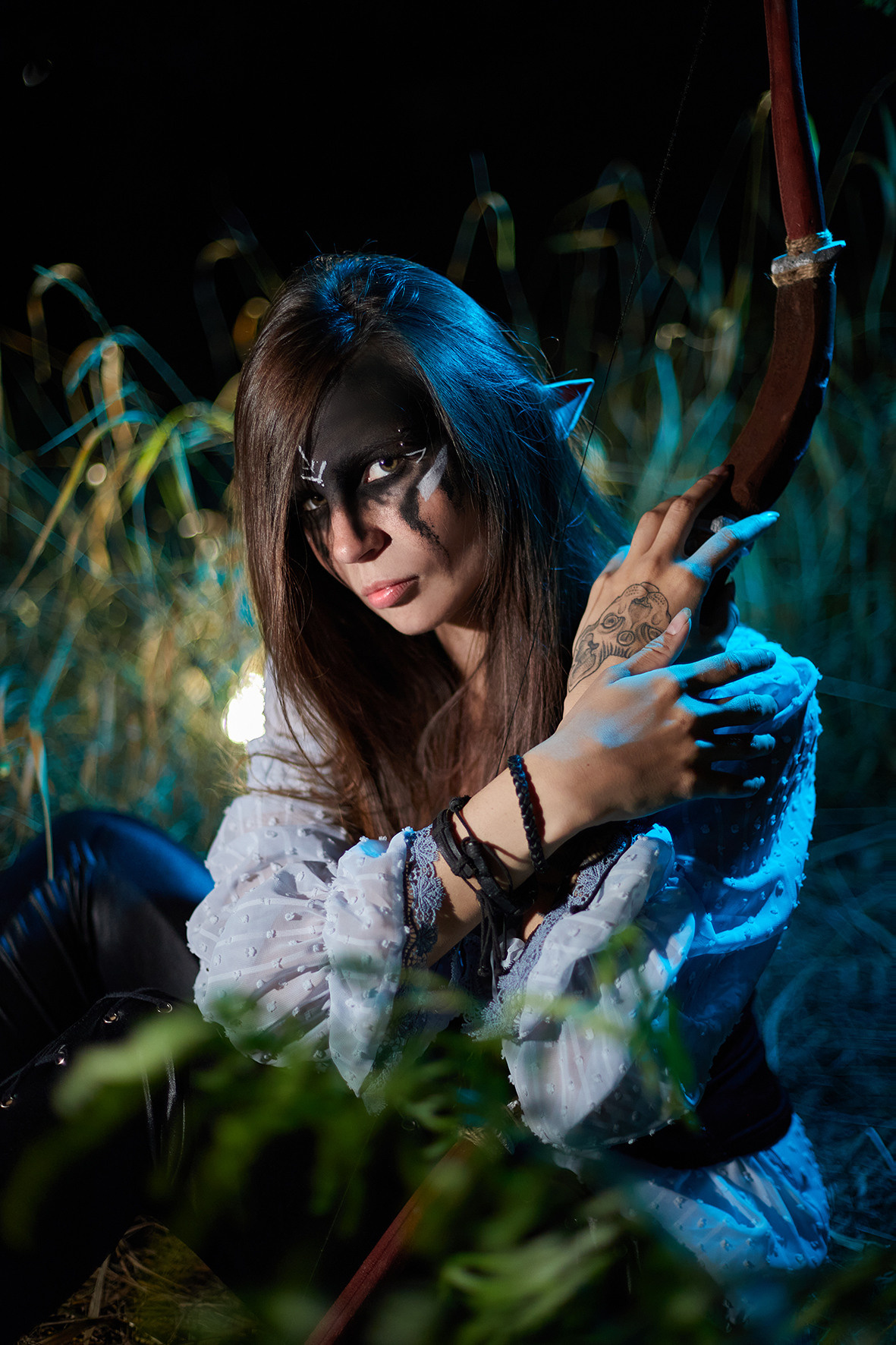 Боевой эльф с черным макияжем с луком и стрелой в руках сидит в высокой траве в ночном лесу. Фотограф. Фотоискусство. Краснодарский край. Кубань. Тимашевск.