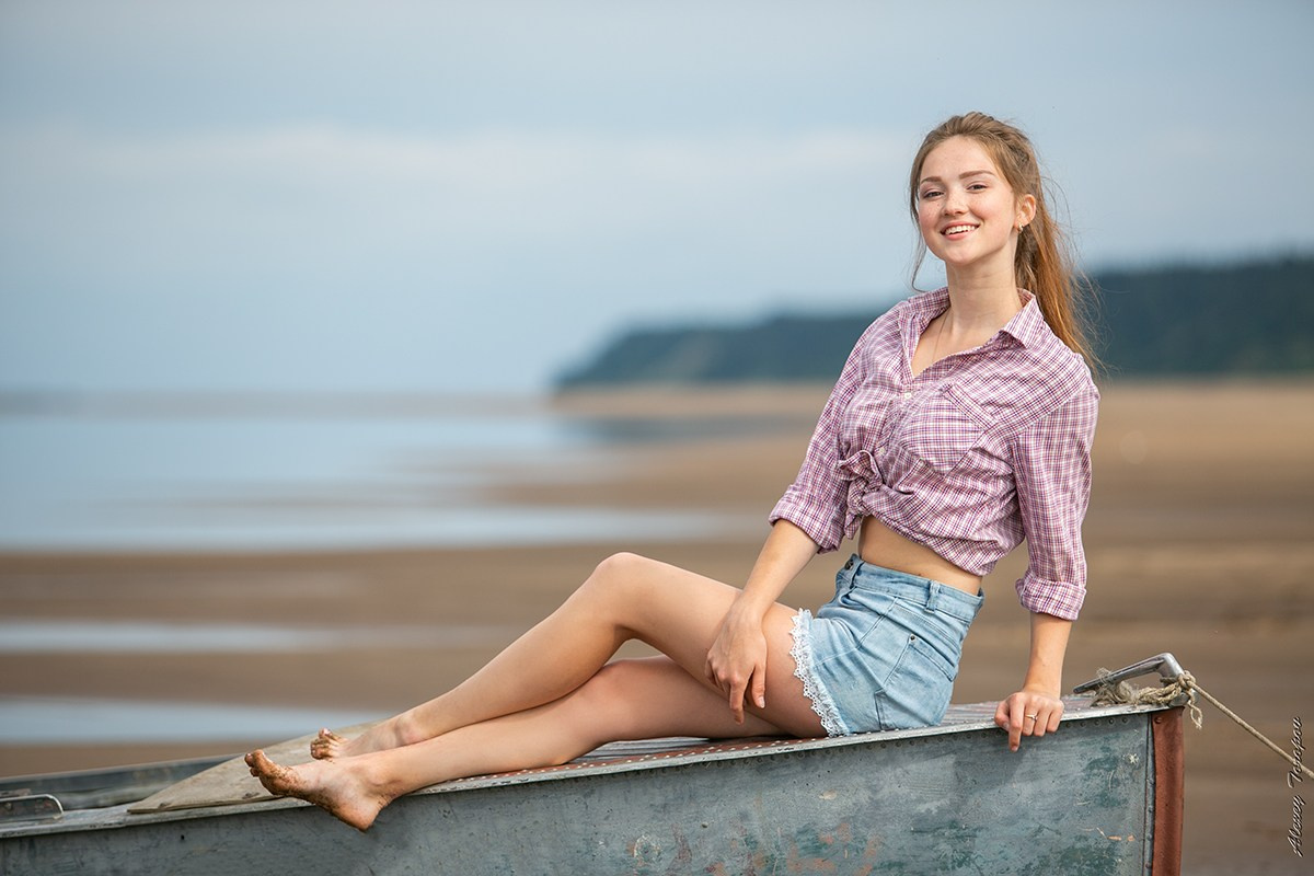 Девушка в шортах позирует на старой лодке на берегу реки