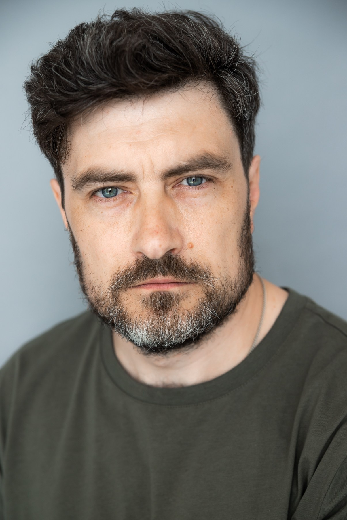 Портрет мужчины с короткой бородой с проседью в зеленой футболке