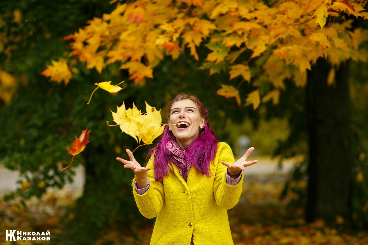 Позитивный портрет веселой девушки , подбрасывающей кленовые листья вверх