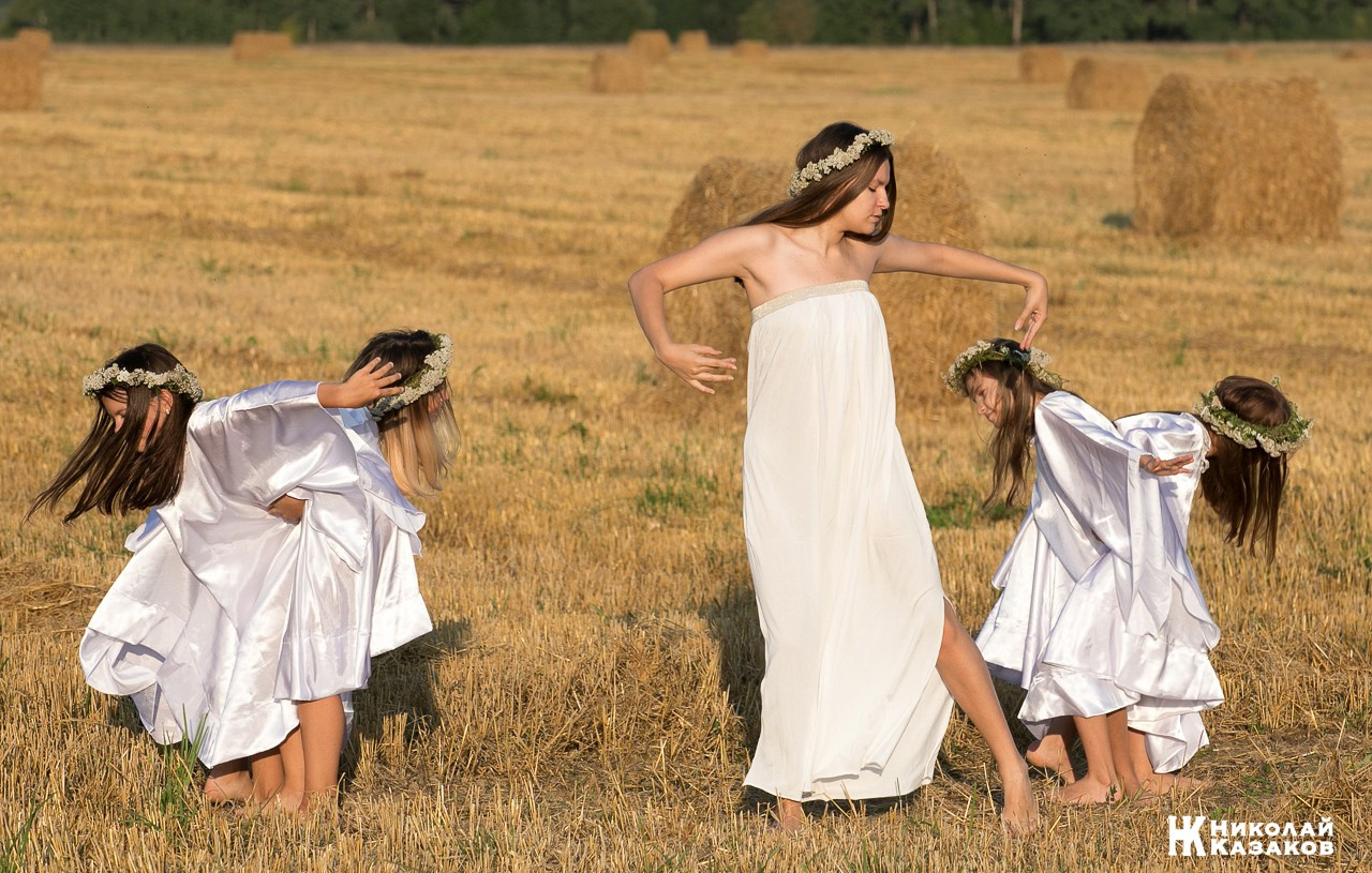 Стройные девочки подростки танцуют в пшеничном поле во время фотосессии на закате.