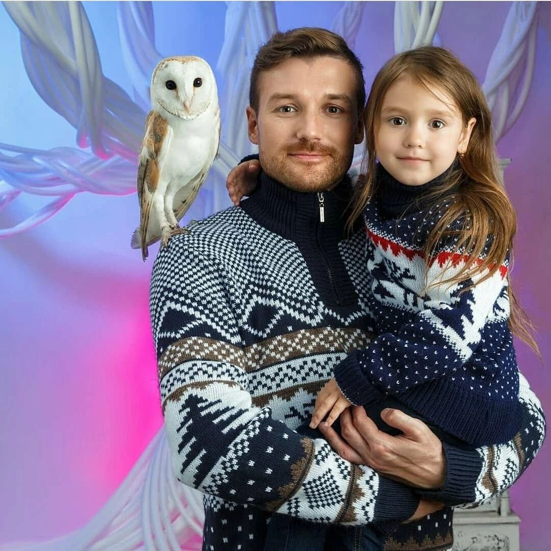 Мужчина в свитере с совой на плече держит девочку на руках