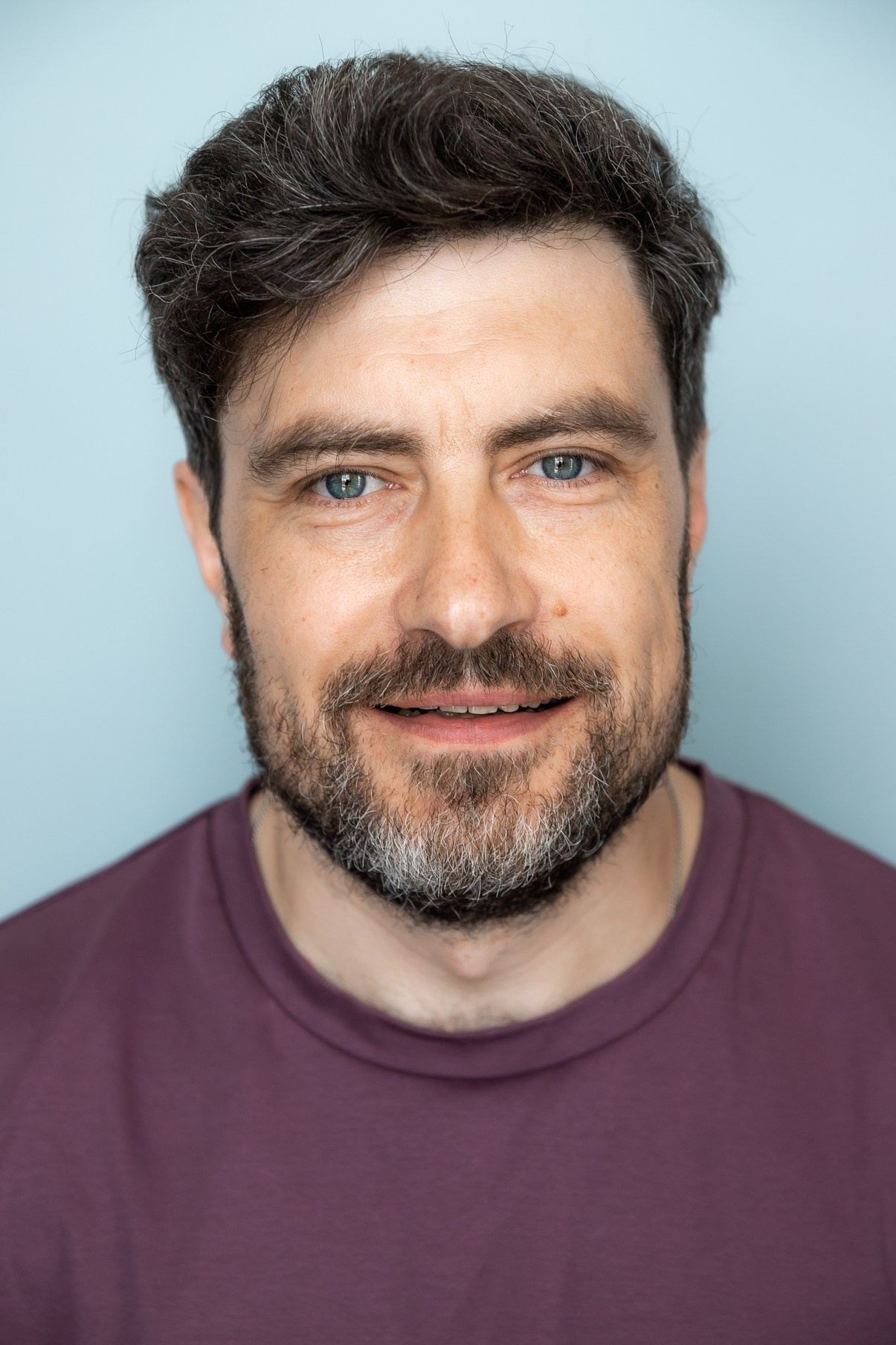 Портрет мужчины с короткой бородой с проседью в фиолетовой футболке