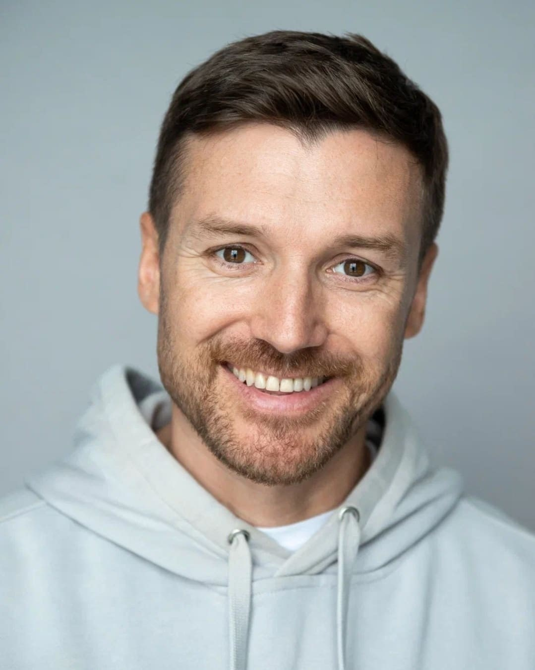 Портрет кареглазого мужчины с короткой щетиной в светлом худи