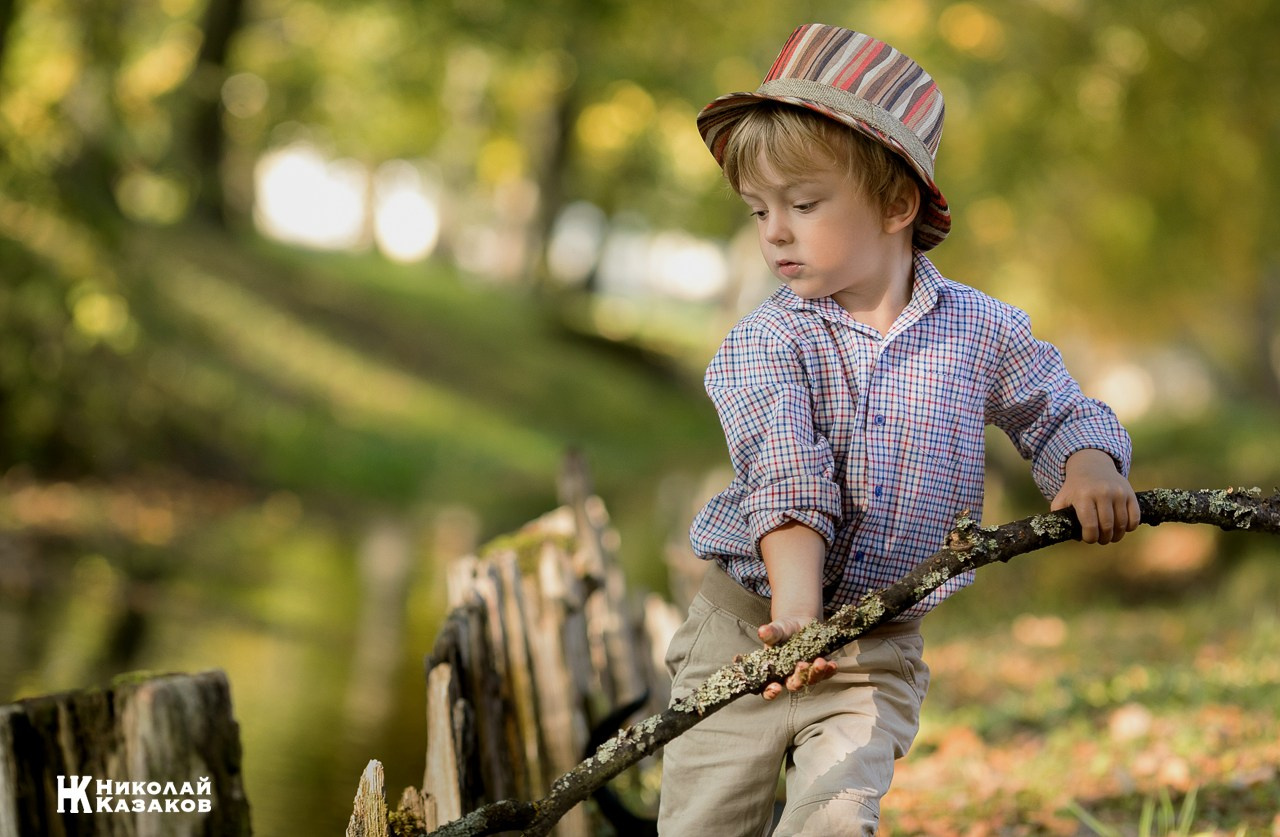Портрет увлеченного маленького мальчика, ловящего палкой водоросли в речке в лучах утреннего солнца
