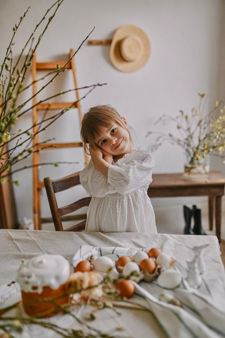 маленькая девочка в белом платье с куличом и пасхальными яйцами