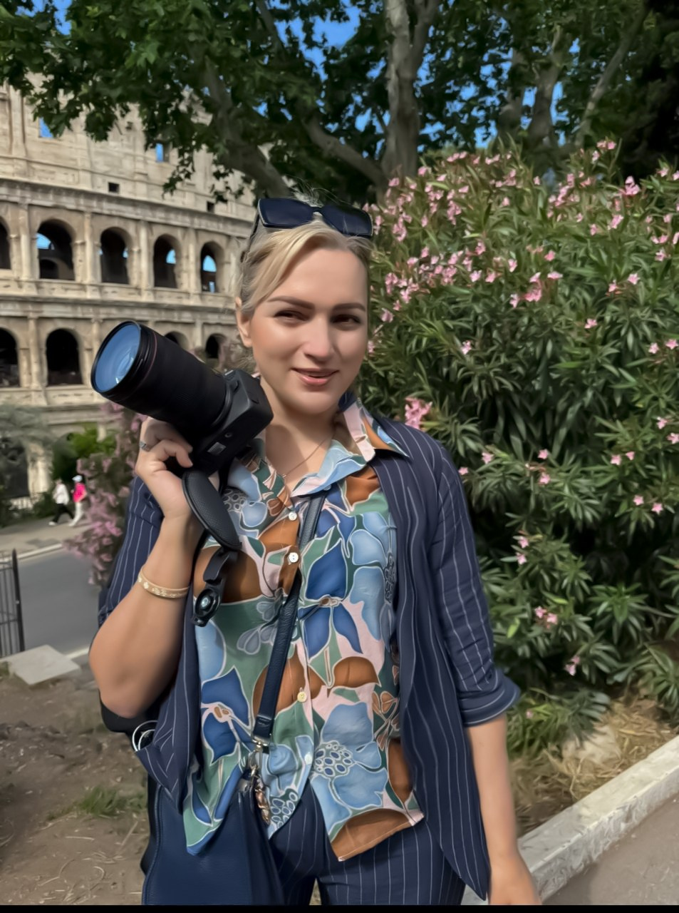 Юлия Перфетти-фотограф держит профессиональную камеру на плече, улыбаясь на фоне исторического Колизея в Риме, Италия.