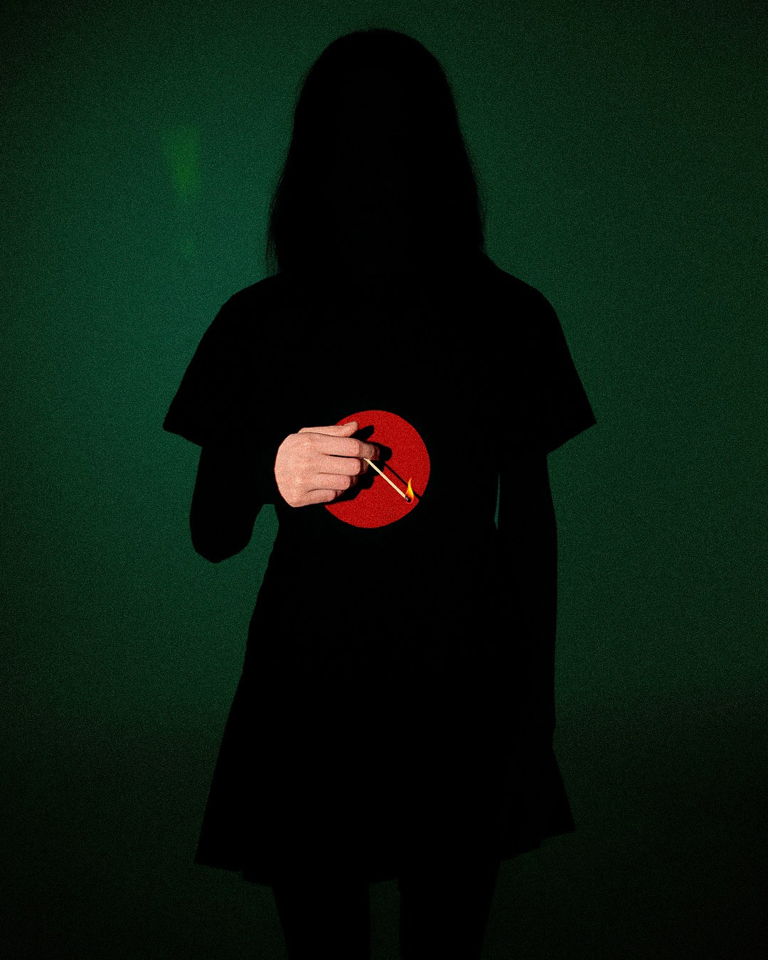 Черный силуэт девушки на зеленом фоне в руке горящая спичка и световой акцент на руке