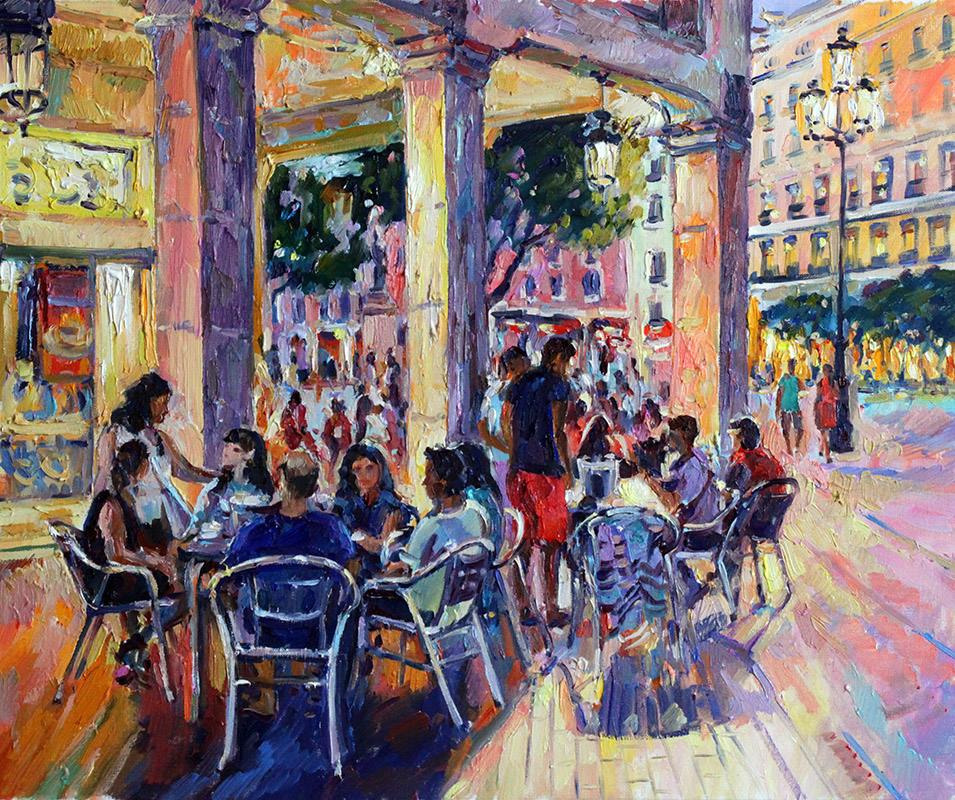 A group of people sitting at tables on the corner of the square.