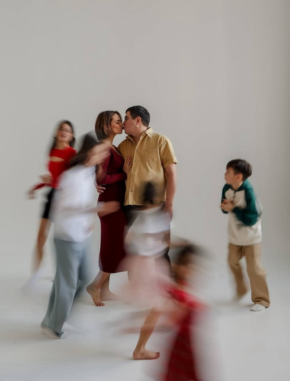 Семья в студии: пара целуется в центре, вокруг — дети, немного размытые. Атмосфера тёплая, живая, весёлая.