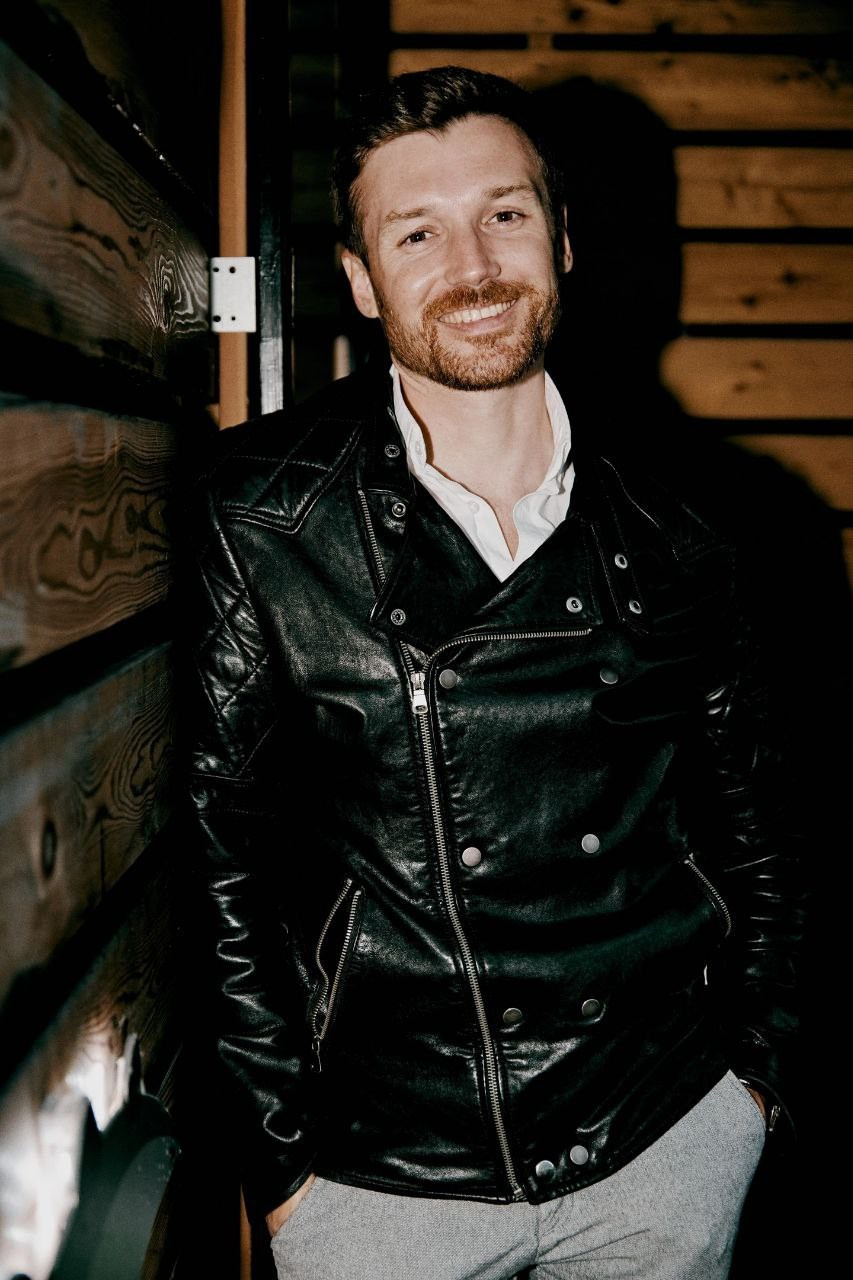 Мужчина с короткой щетиной в кожаной куртке улыбается