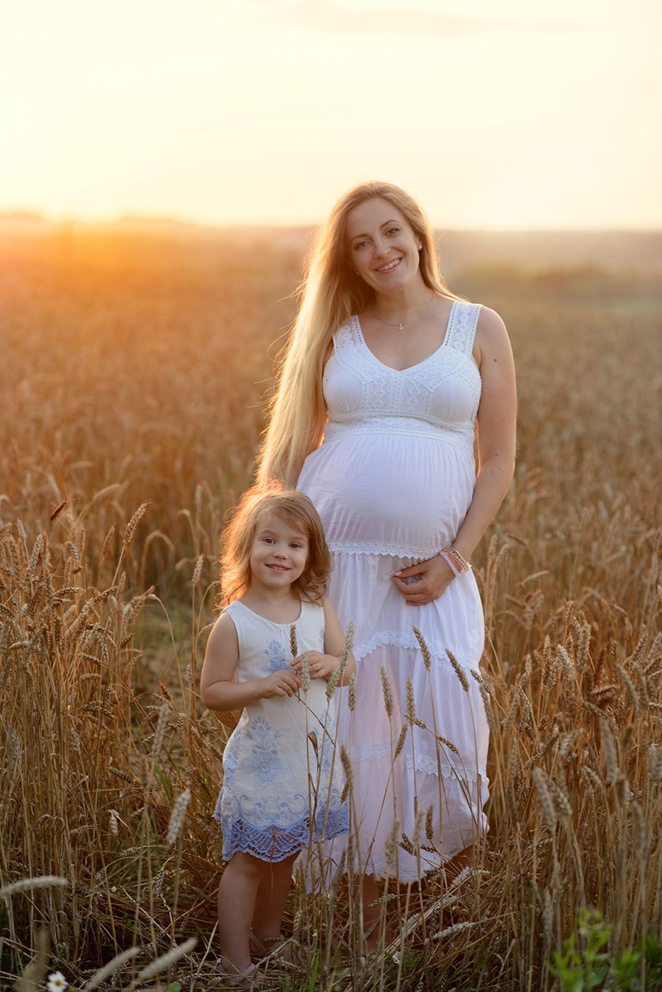 Mom and daughter, Photo shoot, Little girl and a pregnant woman in a wheat field at sunset
