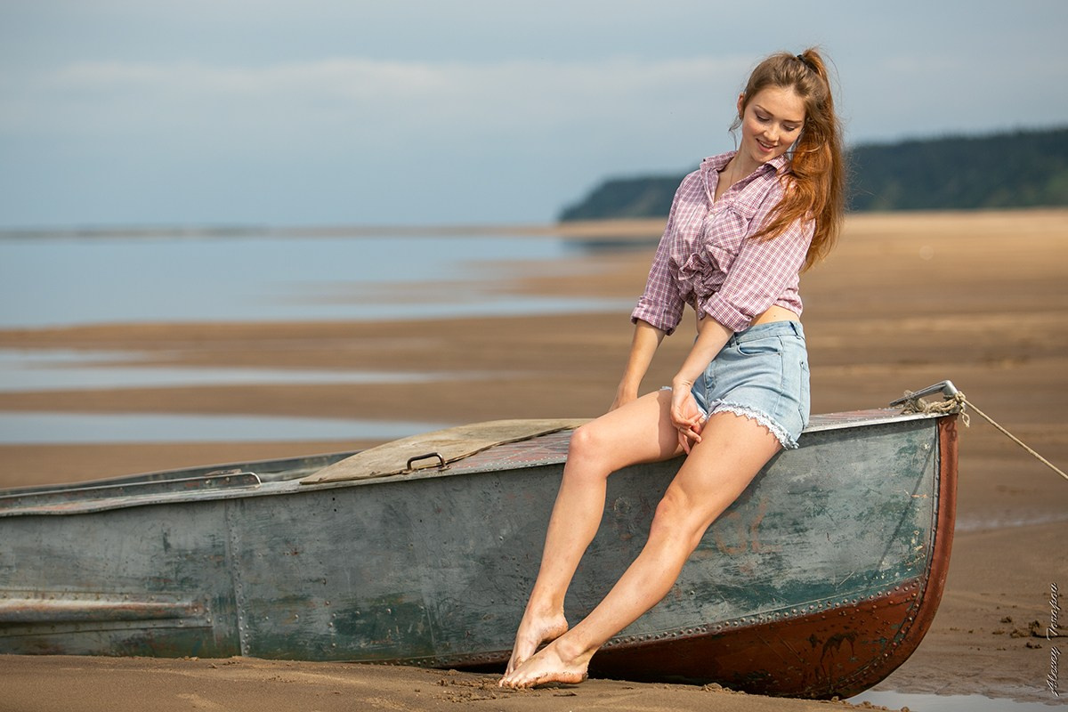 Девушка в шортах позирует на старой лодке на берегу реки