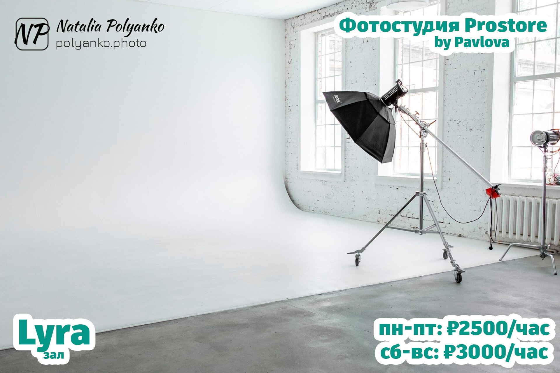 Светлый зал с циклорамой и профессиональным оборудованием. Помещение с белыми стенами и потолком, тремя большими окнами и кирпичной кладкой. В центре — студийный осветитель с большим софтбоксом на штативе с колесиками. В левом нижнем углу указано название зала - Lyra (Лира), в правом верхнем — "Фотостудия by Pavlova", а внизу указана стоимость аренды: пн-пт 2500 руб/час, сб-вс 3000 руб/час.