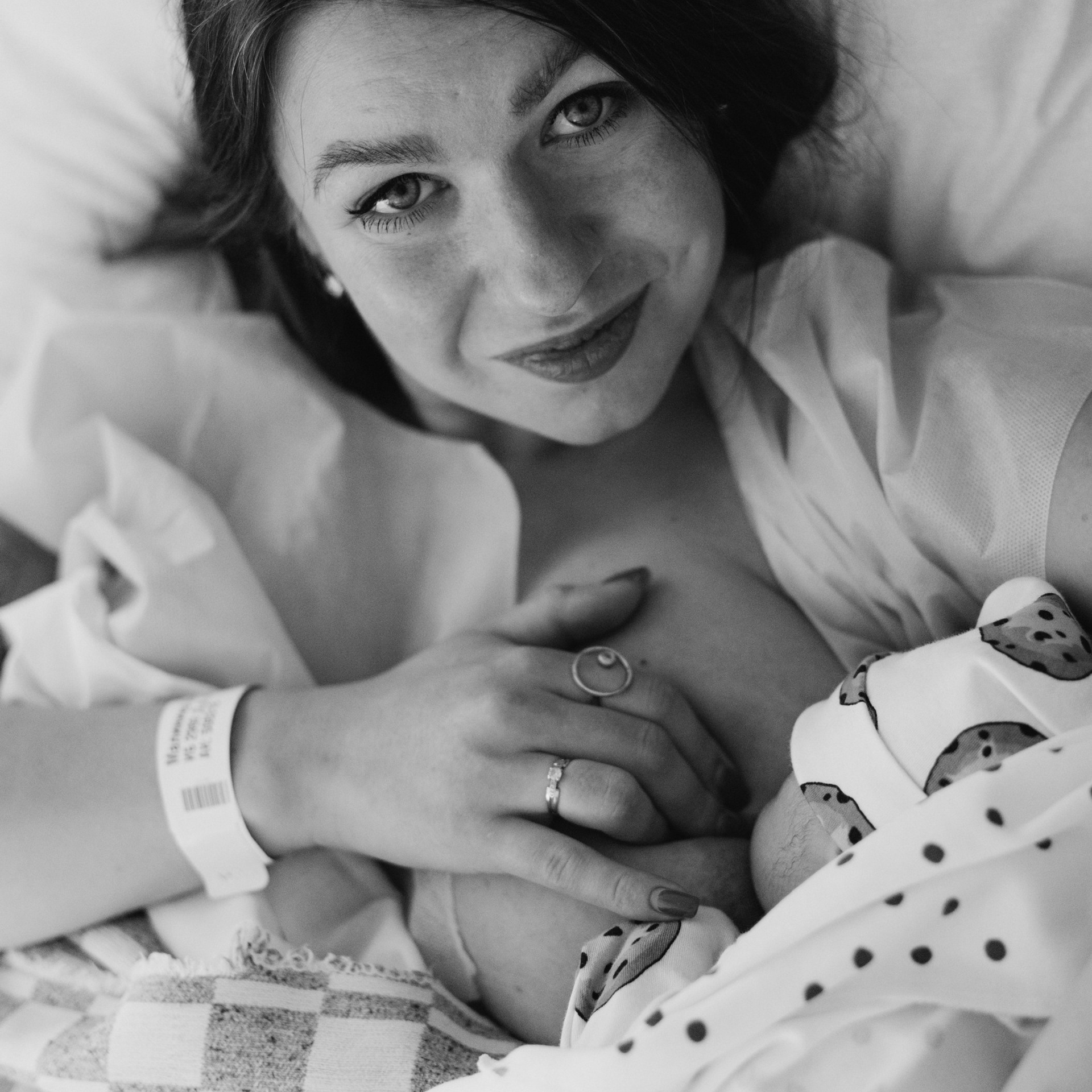 Фото родов. Первое прикладывающие к груди. У мамы на груди лежит малыш. Мама смотрит в камеру. Улыбается