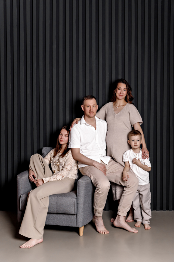 Семья из четырёх человек: мужчина, женщина, девочка и мальчик. Сидят и стоят у тёмной стены в студии.