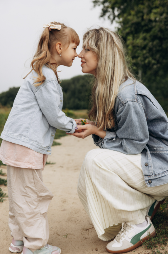 Мама и дочка на природе: мама присела на корточки, они смотрят друг другу в глаза, атмосфера тёплая и нежная.