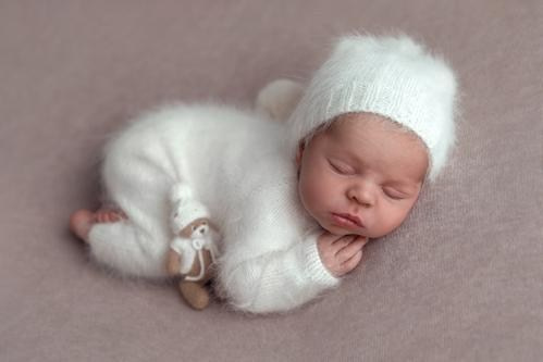 ньюборн фотосессия малыша в белом пушистом комбинезончике и колпачке с мишкой в шапочке