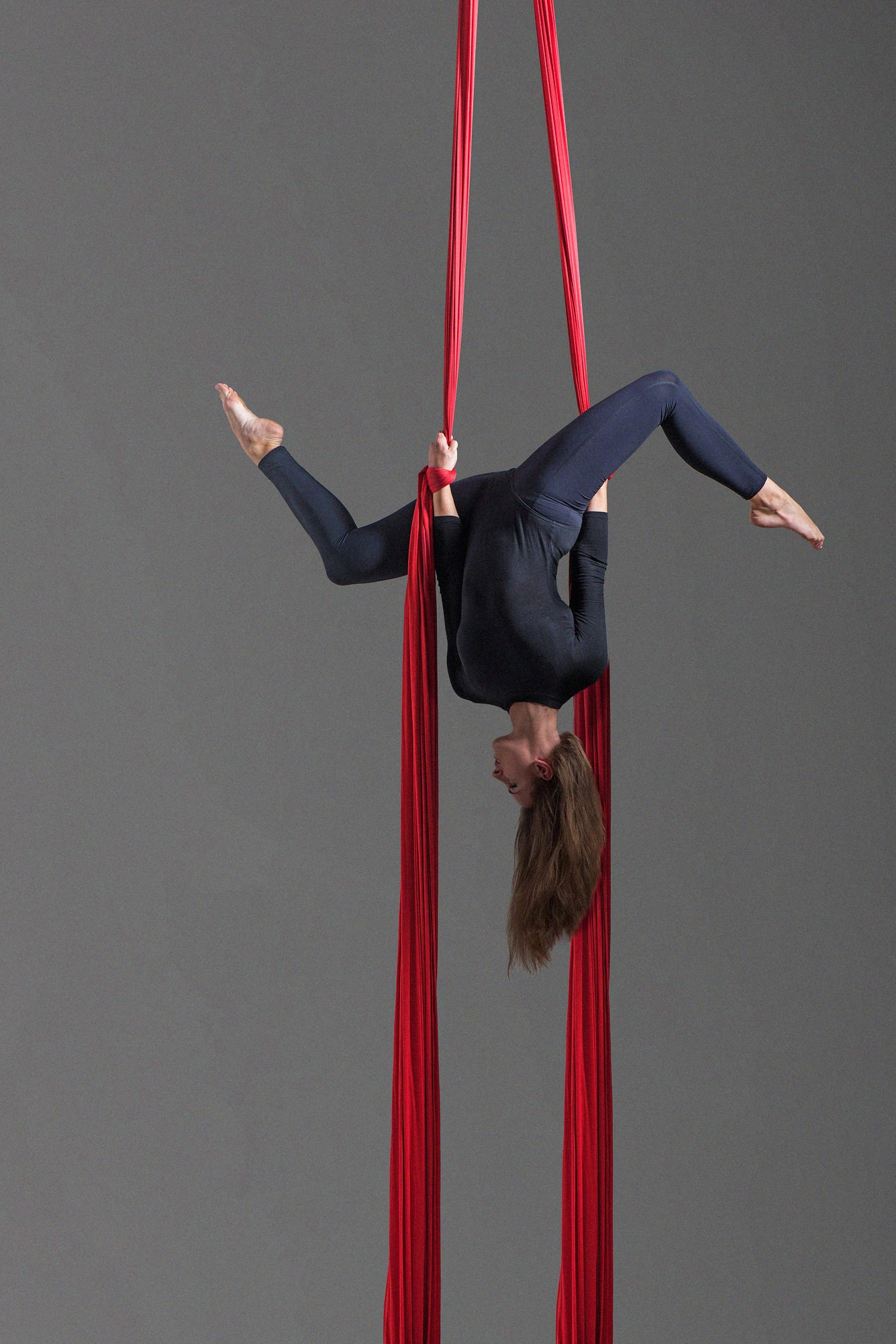 Гимнастка вытягивается в вертикальную фигуру, удерживаясь на полотнах и создавая плавный изгиб корпуса. Работа света подчёркивает силу и гибкость. Студийная съёмка воздушной гимнастики, Москва и Истринский район.