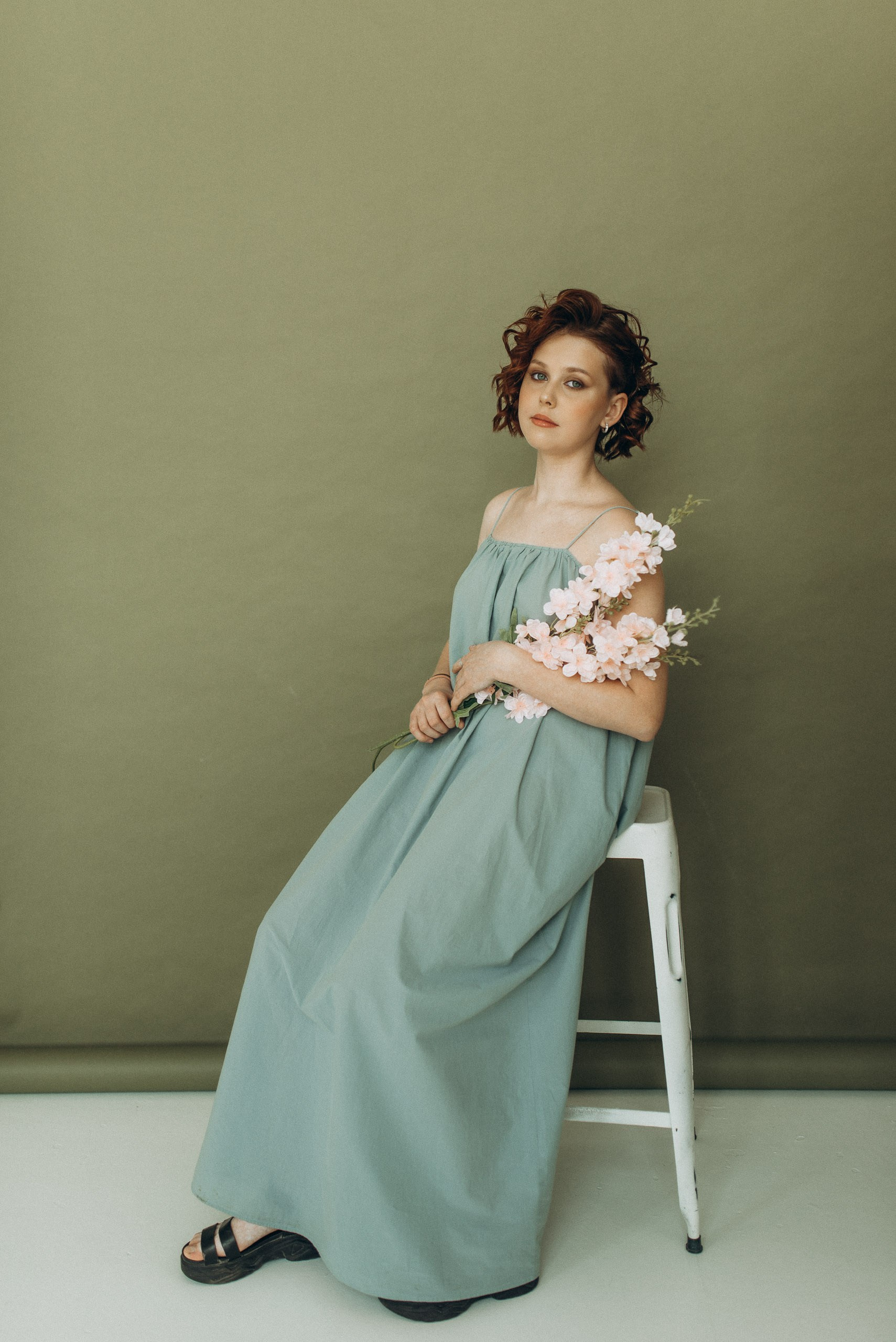 Девушка в длинном голубом сарафане с веткой розовых цветов. Фотосессия в студии на зеленом фоне, подростковый портрет в Новосибирске