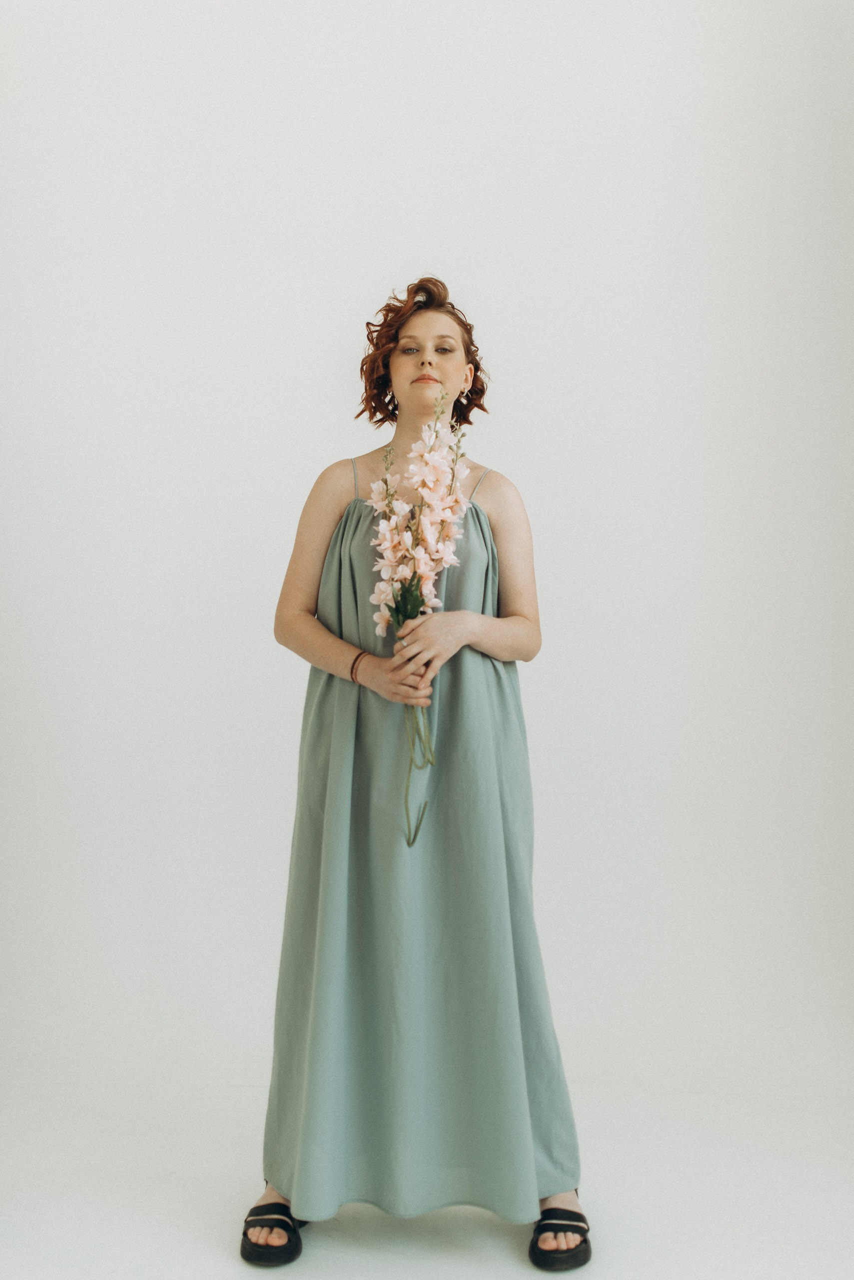 Девушка в длинном сарафане с цветами в руках. Портрет в полный рост в светлой циклораме. Профессиональный подарок на 15 лет