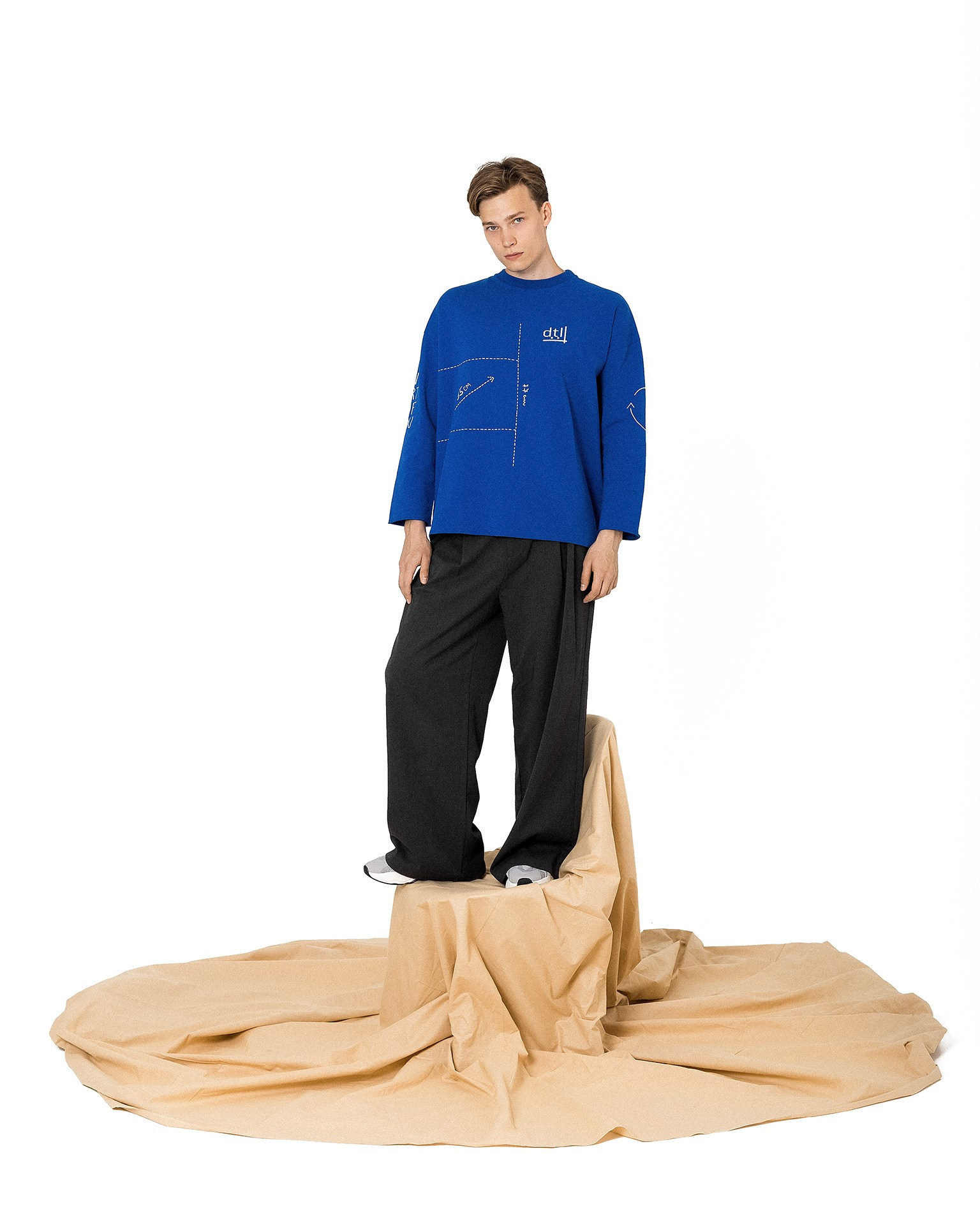 Креативная съемка одежды с моделью в студии Казань, молодой парень в стильной брендовой одежде стоит на стуле с бежевой тканью на полу