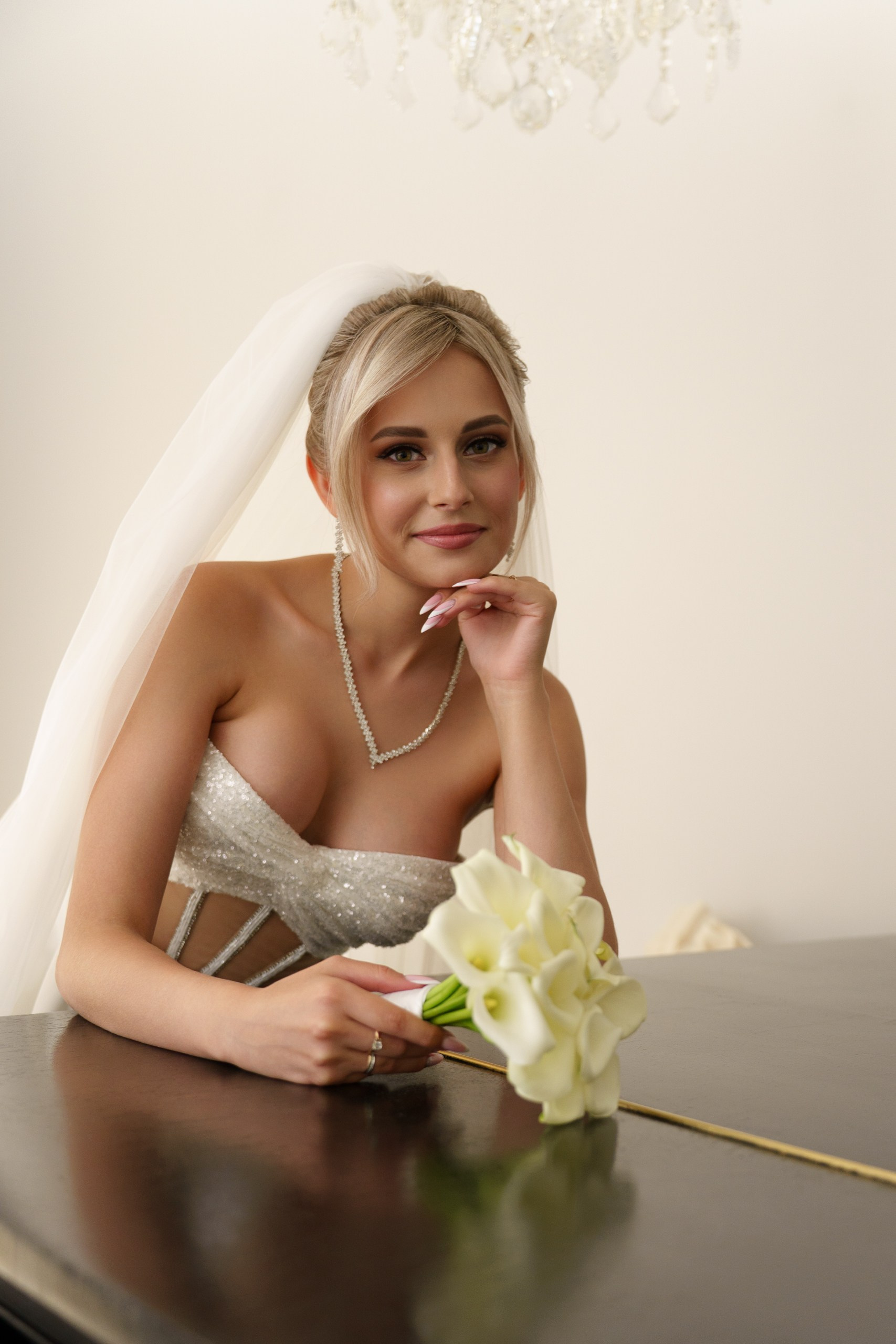 Свадебная фотография: невеста в сверкающем платье, с фатой и жемчужными украшениями, позирует с букетом белых калл. Её поза и выражение лица передают нежность и радость момента | фотосессия с букетом невесты Екатеринбург
