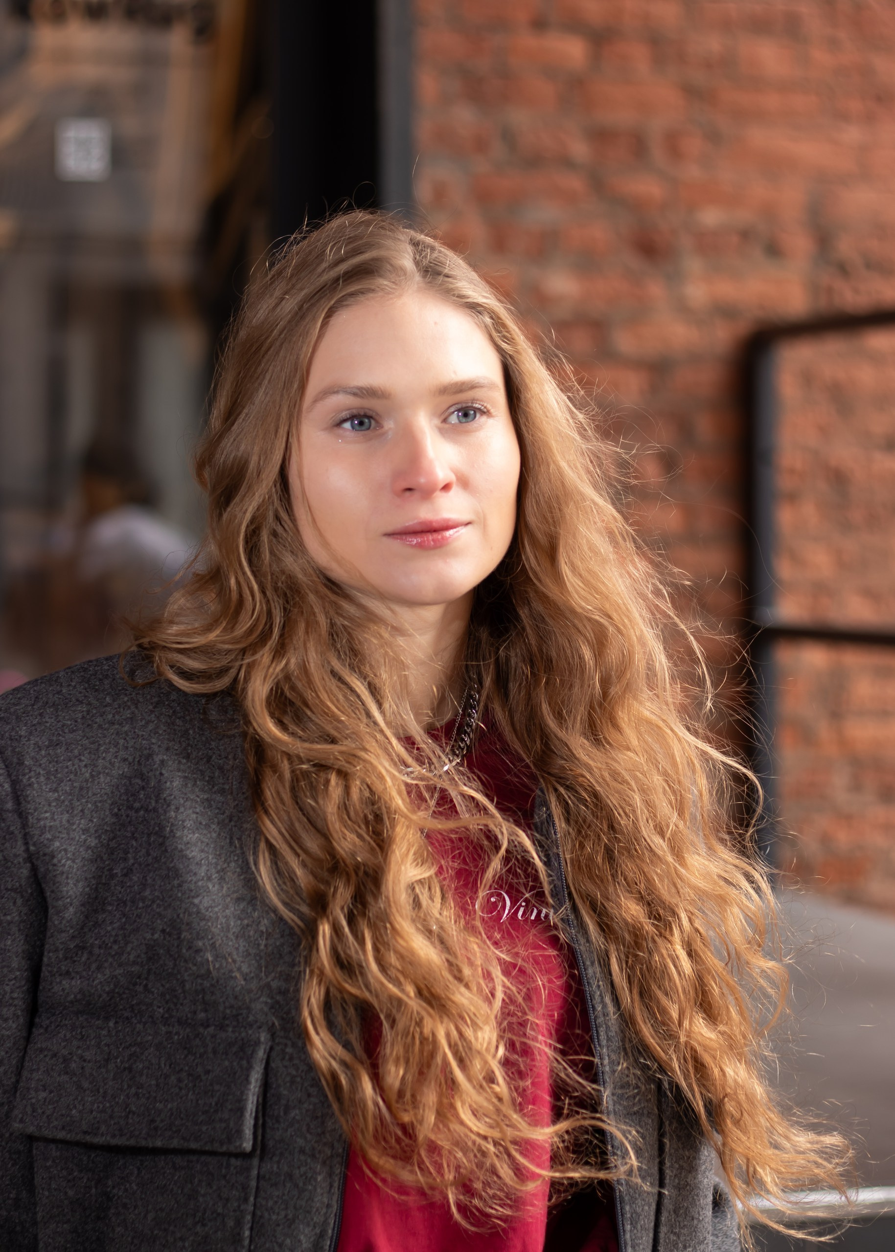 Осенняя уличная фотосессия девушки с длинными волосами у кирпичной стены — фотограф Карасёва Елена