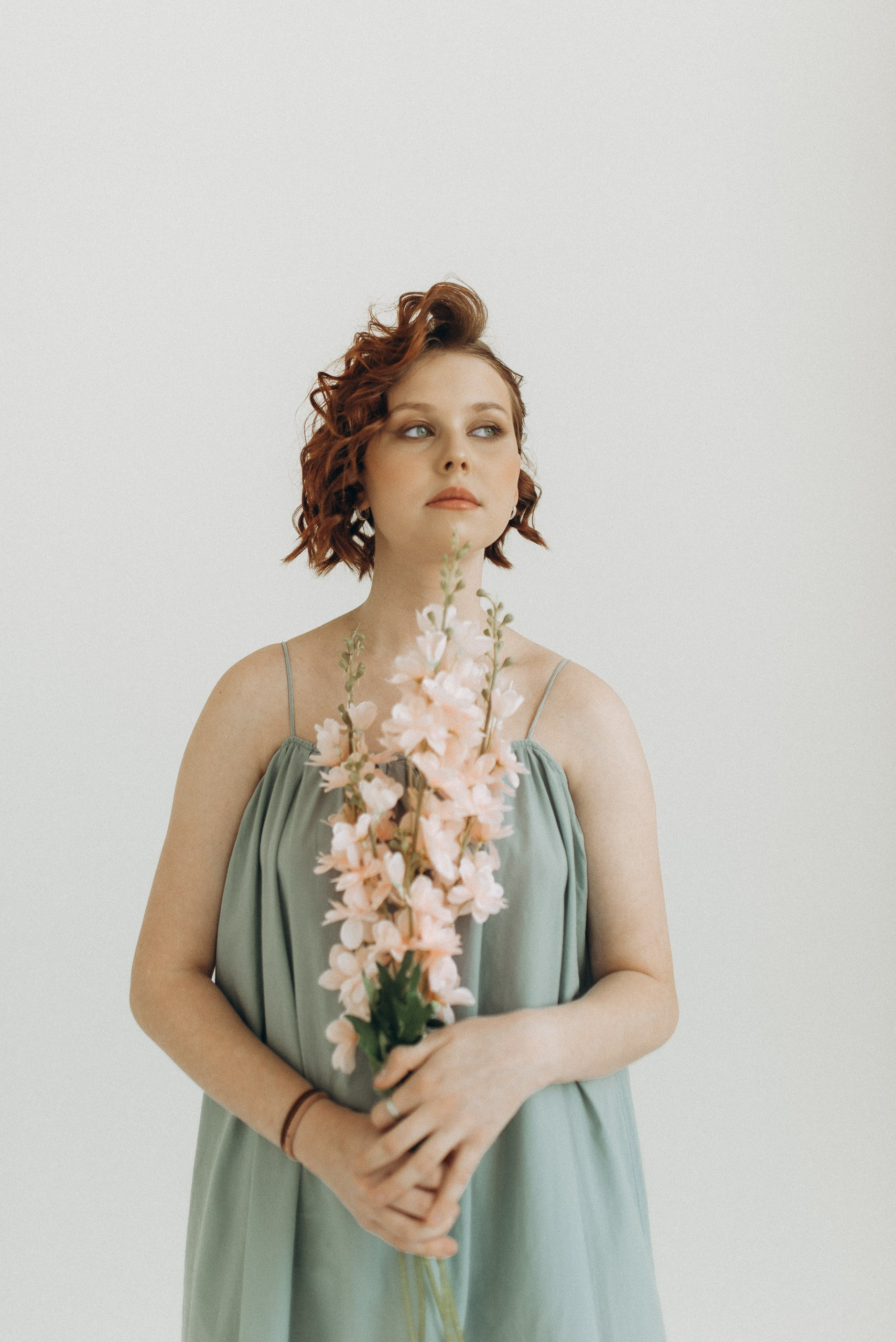 Портрет девушки с веткой цветов на светлом фоне. Нежный образ, рыжие локоны и голубое платье. Студийная съемка в Новосибирске