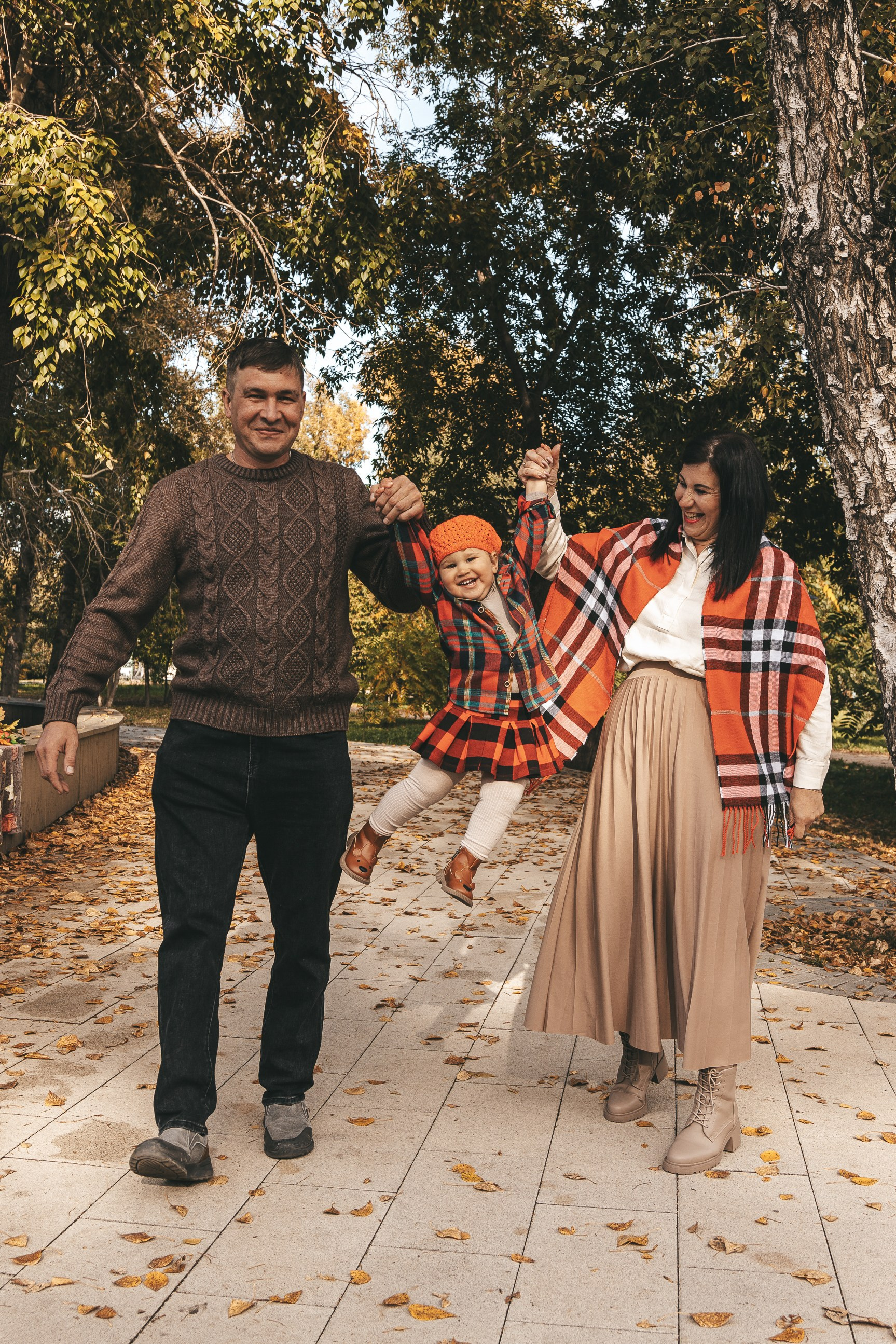 Родители держат детей за руки и идут по аллее парка.