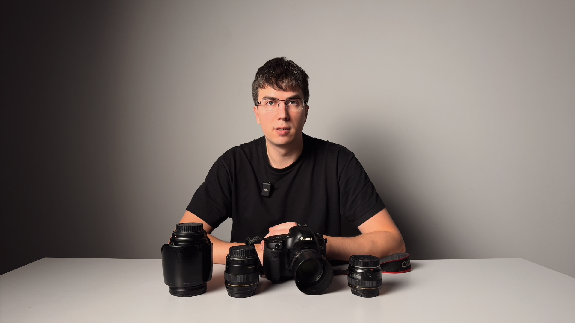 Камера Canon и сменные объективы на столе перед преподавателем — фрагмент видеоурока о съёмке на фотозоне со вспышкой.
