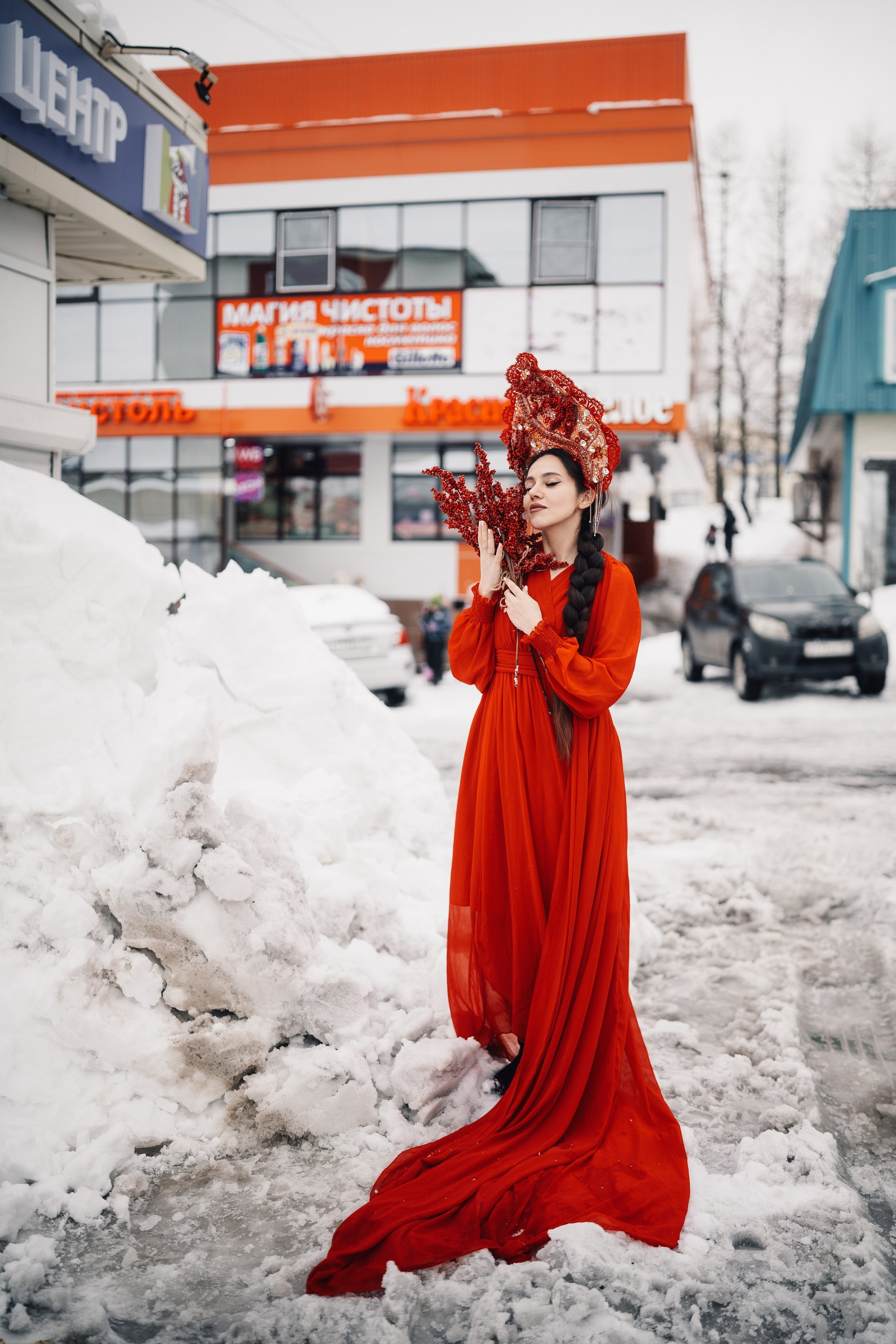 Девушка в красном платье в образе весны на фоне тающего снега в городе, уличная фотосессия весной, контрастный художественный портрет