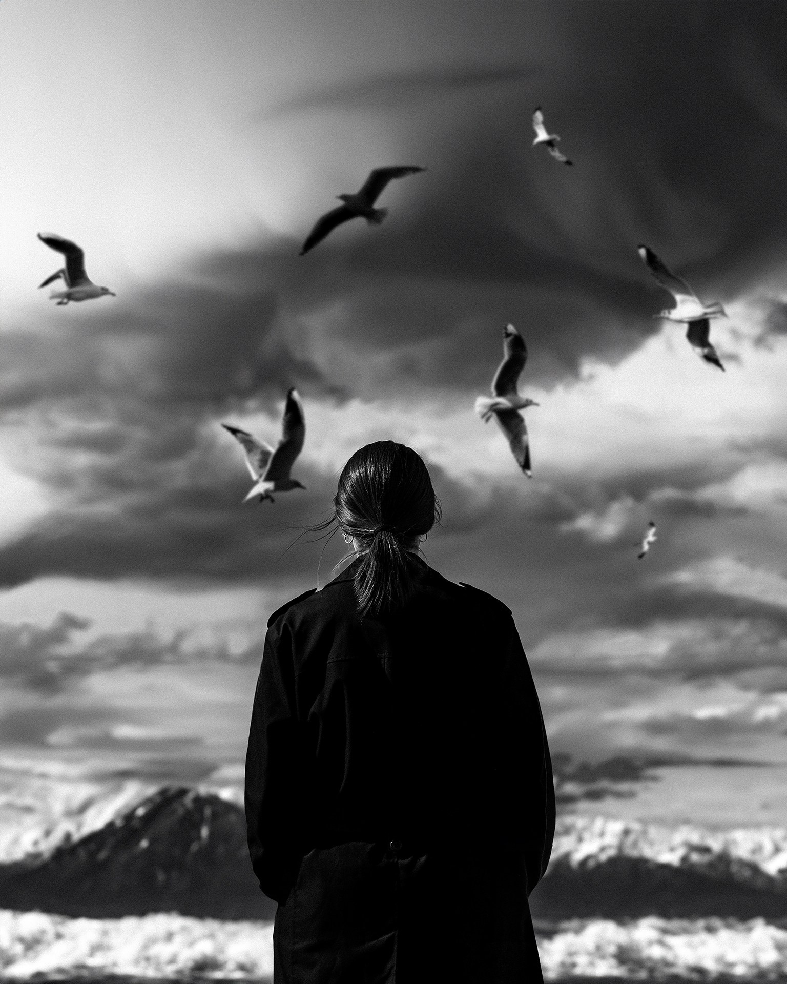 Девушка в пальто стоит на фоне моря и гор вокруг неё летают чайки, уличная съемка Казань