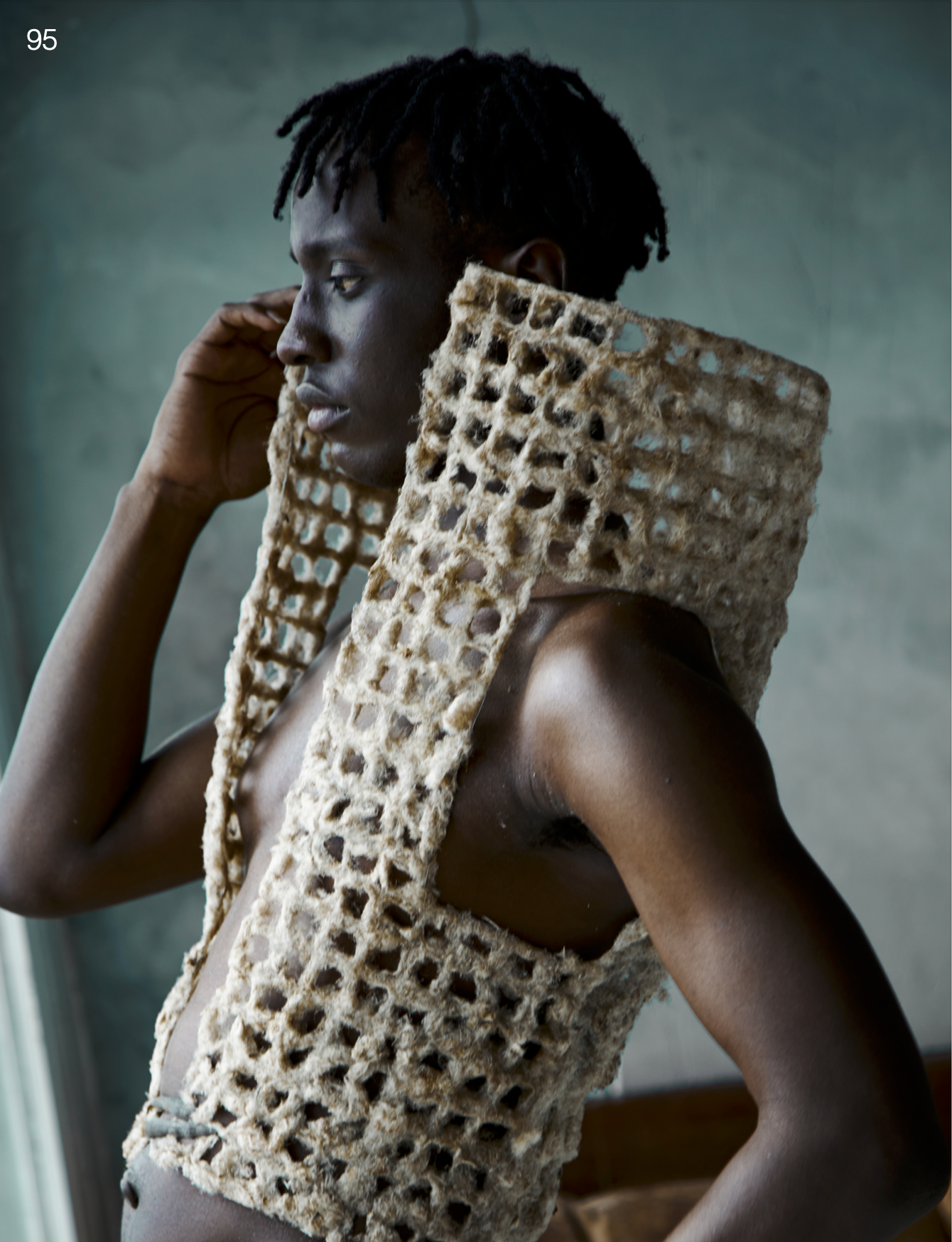 Profile portrait of a Black male fashion model wearing an experimental geometric vest made from organic woven material, contemporary fashion editorial
