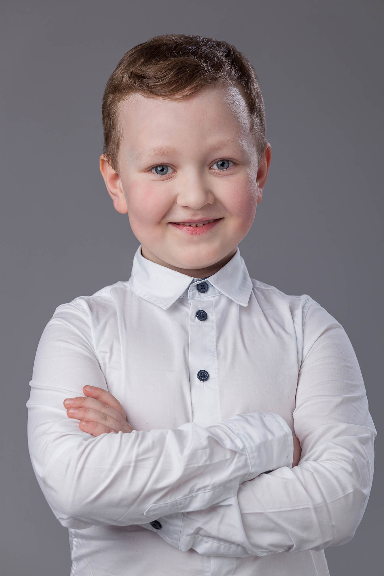 Поясной портрет улыбающегося выпускника детского сада в белой рубашке со скрещенными руками на груди.