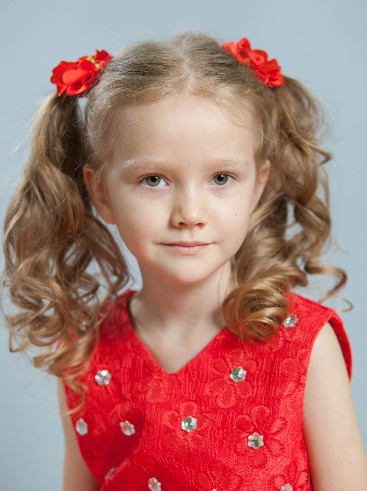 Подгрудный портрет выпускницы детского сада в красном платье и красными резинками в волосах.