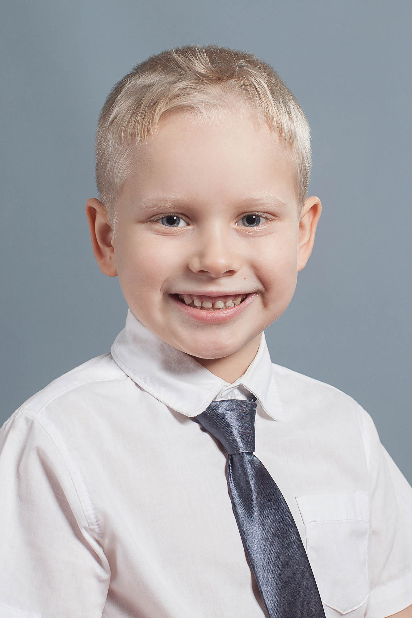 Портрет выпускника детского сада в белой рубашке и сером галстуке на сером фоне.