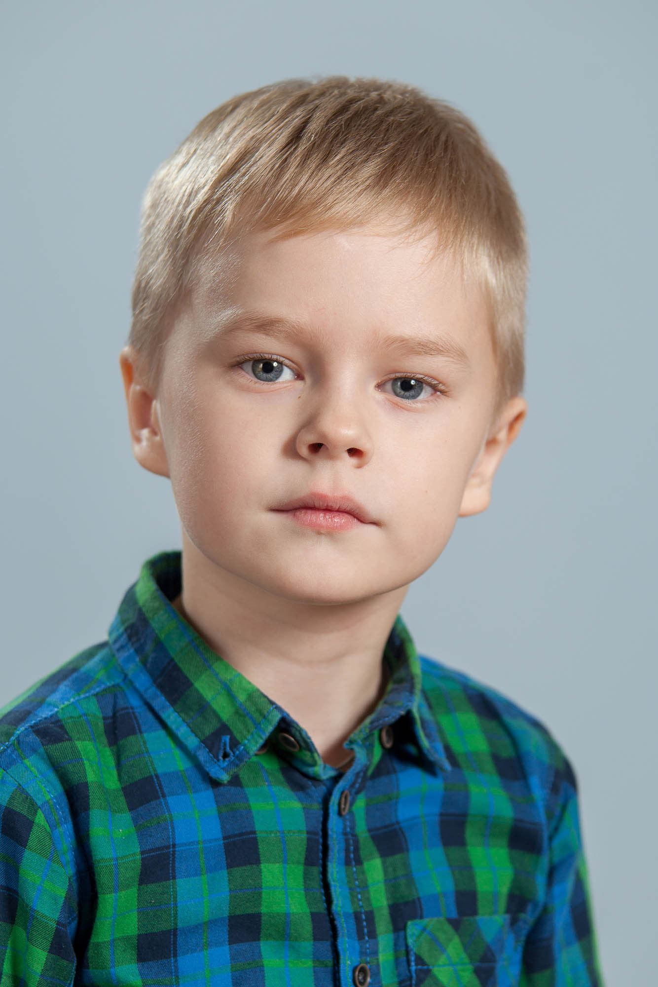 Портрет выпускника детского сада на сером фоне в зеленой рубашке в клеточку.