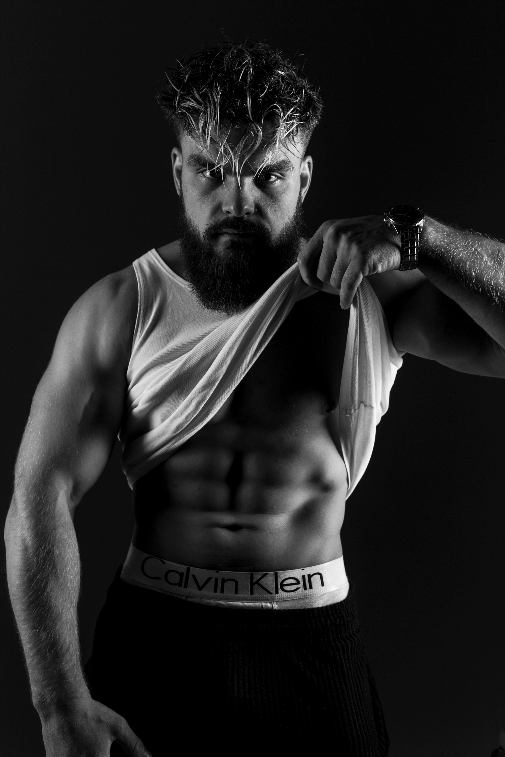 Мужская фотосессия в черно-белом: модель с рельефным прессом и бородой, свет сбоку, руки за спиной — драматичный портрет силы, съемка в Минске