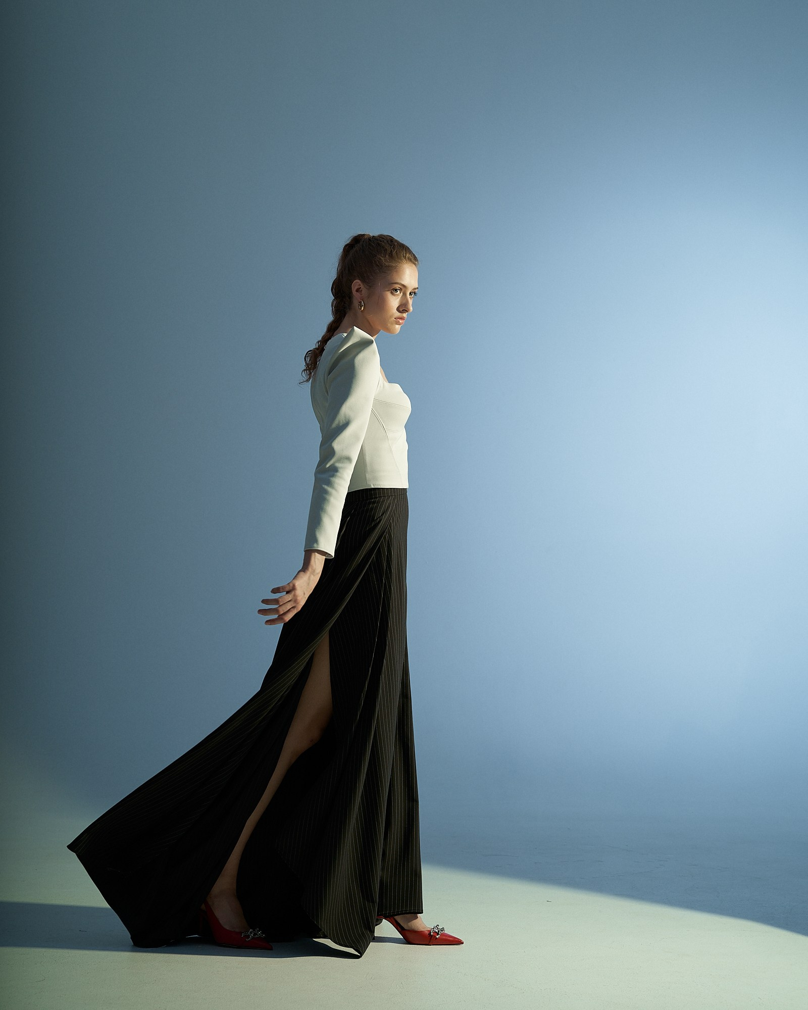 Fashion-съёмка модели в длинной юбке и белой блузе на фоне градиентного студийного света