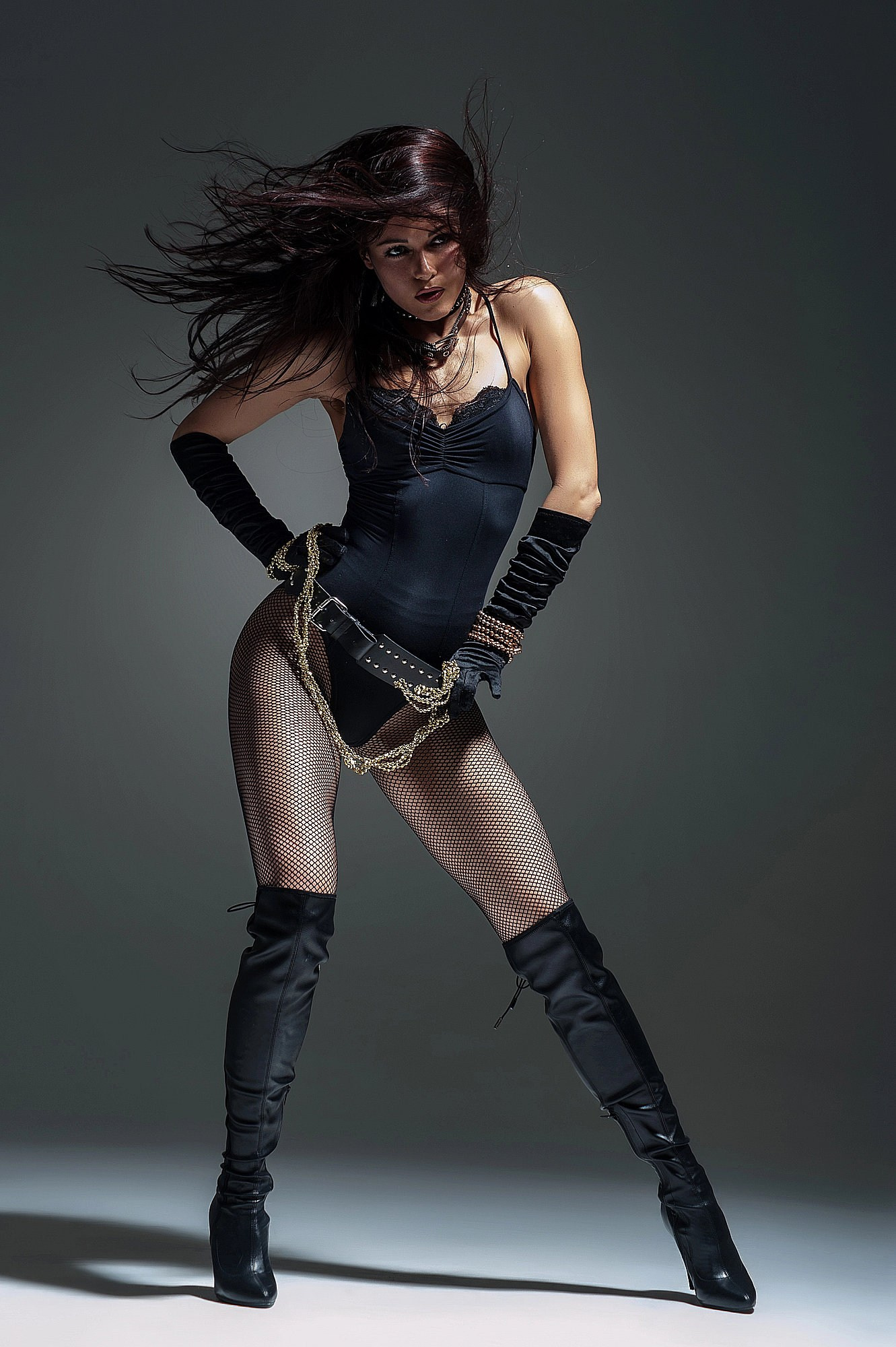 Танцовщица переносит вес на одну ногу и формирует выразическую S-линию корпуса. Чёрный костюм подчёркивает силу ног, а свет выделяет текстуру кожи и костюма. Шоу-эстетика и современный танец. Профессиональная съёмка, Москва и Истринский район.