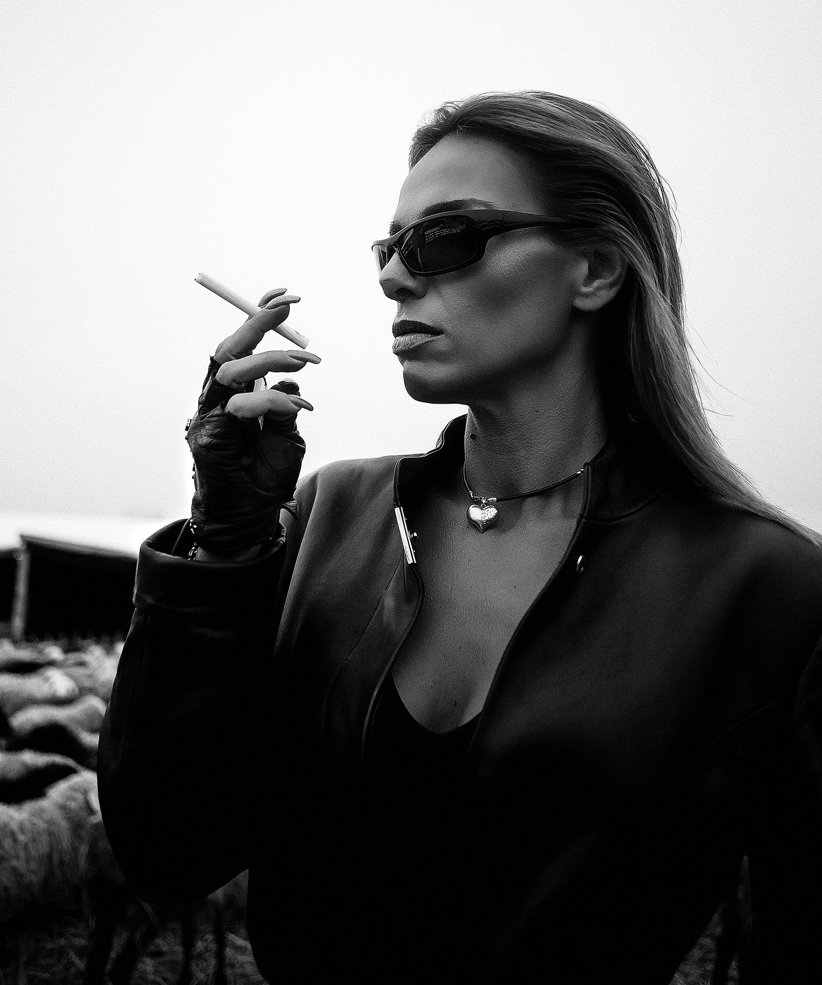 Фэшн в загоне с овцами Казань, девушка в модном образе в плаще и черных очках позирует в загоне овец на ферме