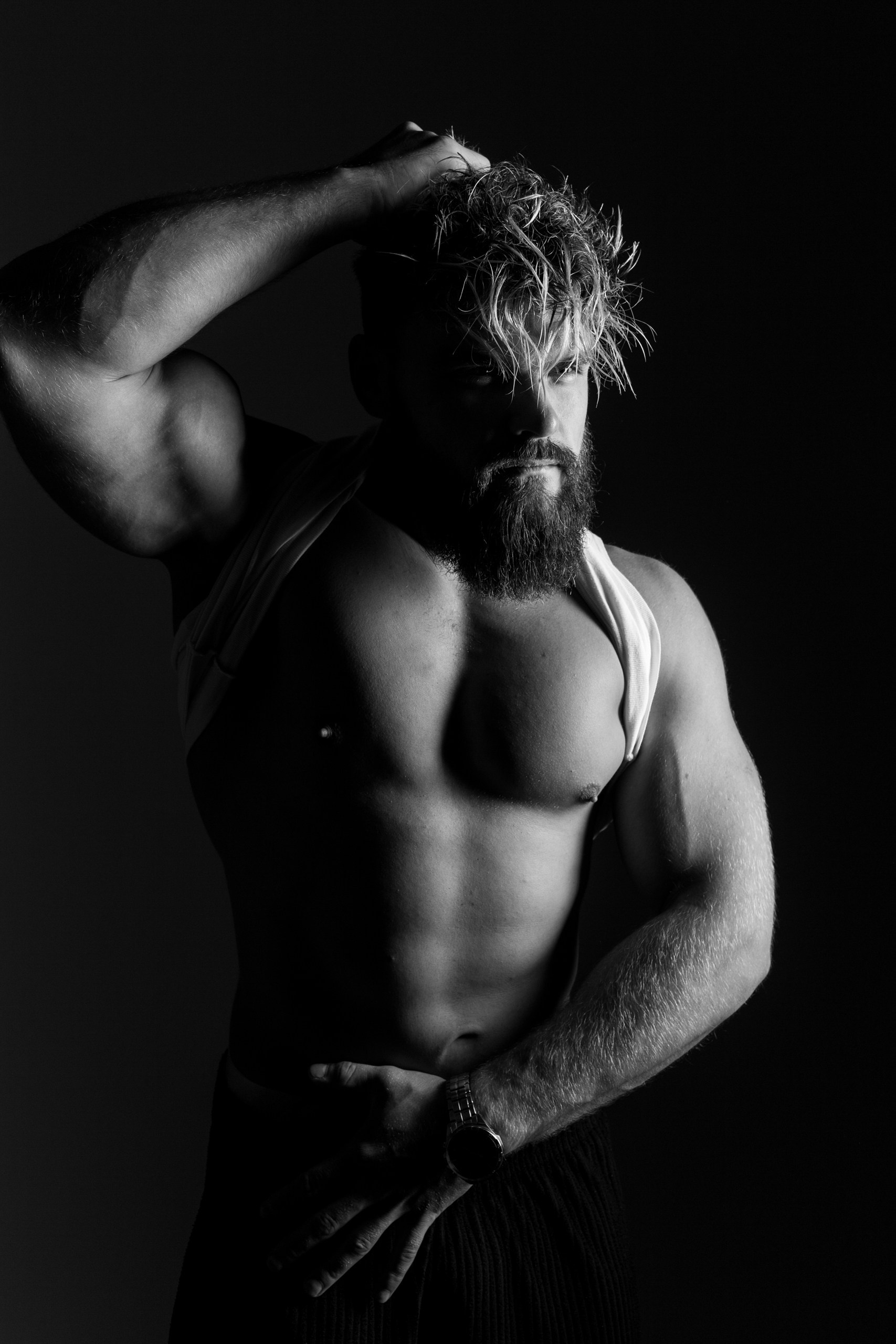 Съемка в низком ключе: мужчина с густой бородой и волнистыми волосами, свет подчеркивает рельеф пресса и ключицы, Минск