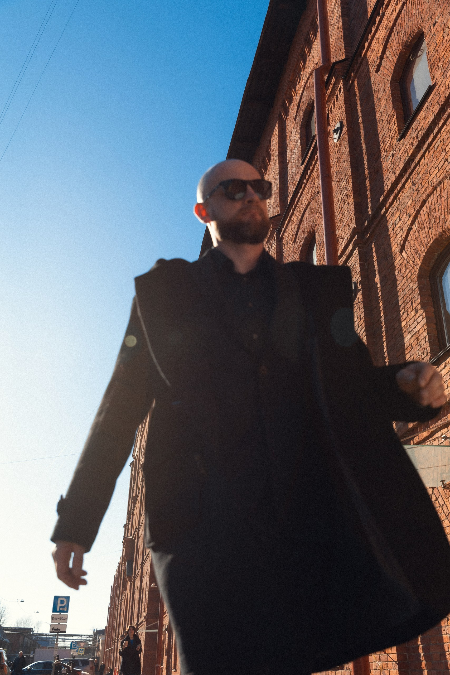 Крупный план мужчины в очках и пальто на фоне кирпичной стены, уличная фотосессия в Санкт-Петербурге.