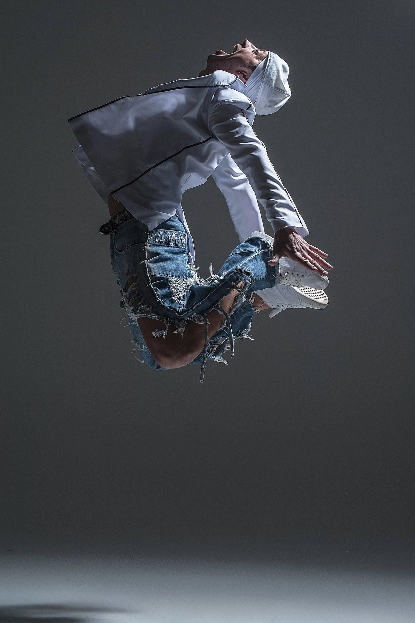 Стрит-танцор зависает в воздухе, выполняя вращение корпуса в прыжке. Сцена снята в динамичном контровом свете. Профессиональная танцевальная фотосъёмка в Москве и Истринском районе.