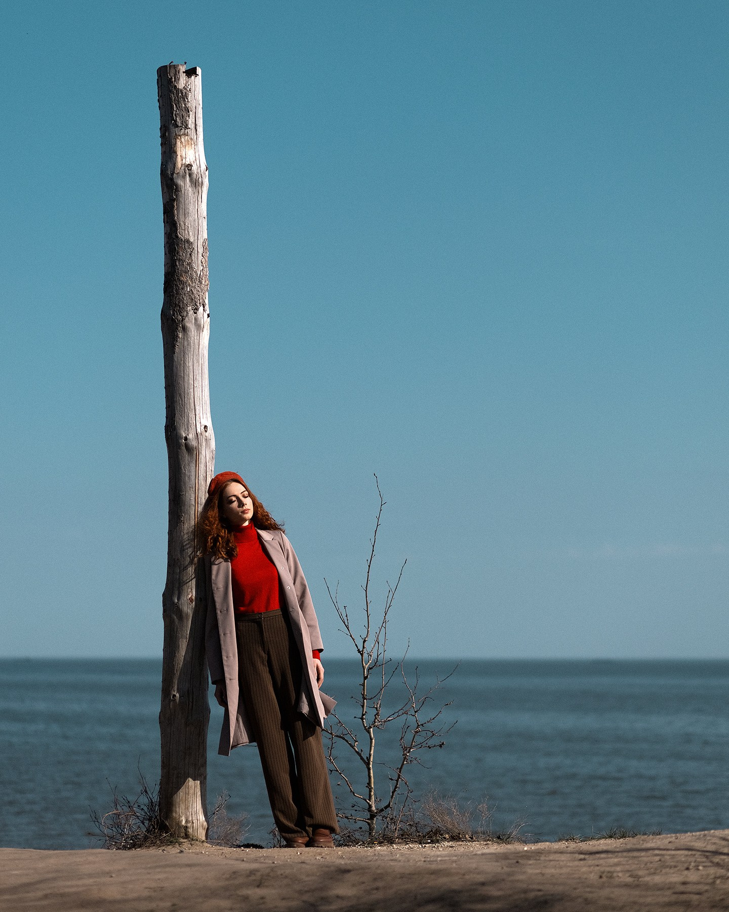 Молодая девушка позирует со столбом дерева на фоне моря